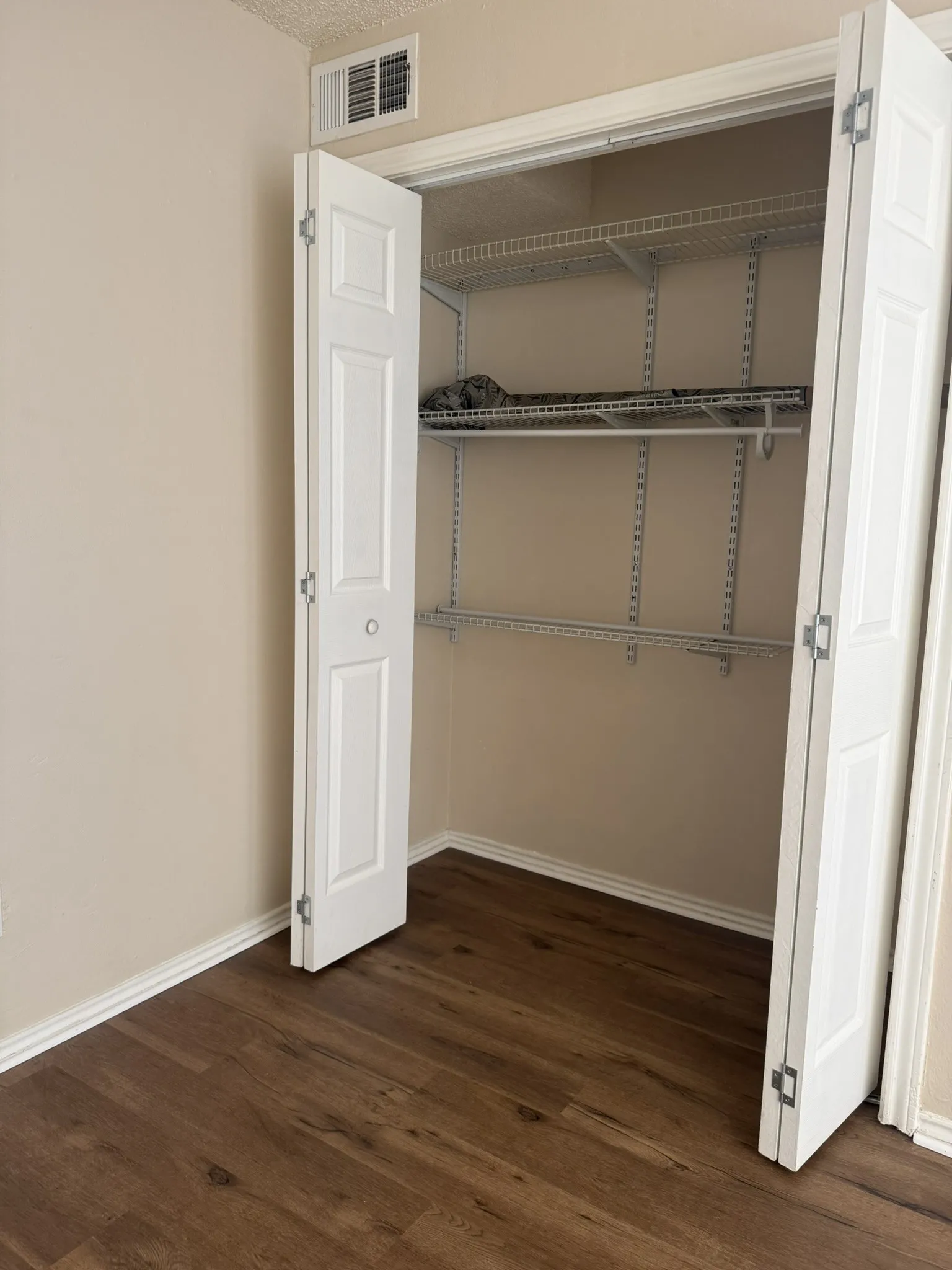 Closet featuring white bi-fold doors and dual-level wire shelving over wood-finish flooring