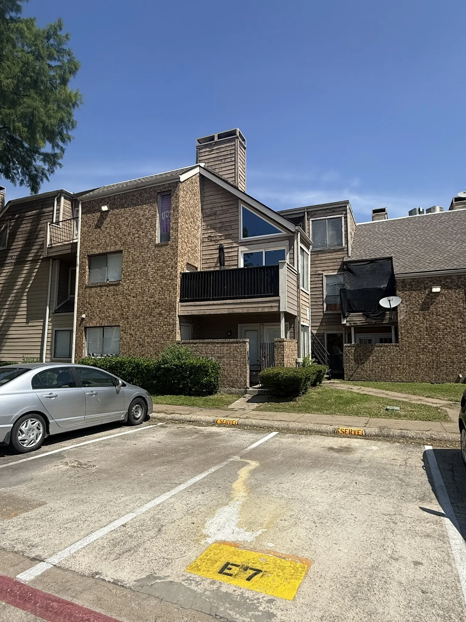 Exterior building facade featuring textured masonry siding, a gabled roofline, an elevated balcony with railing, and a chimney stack