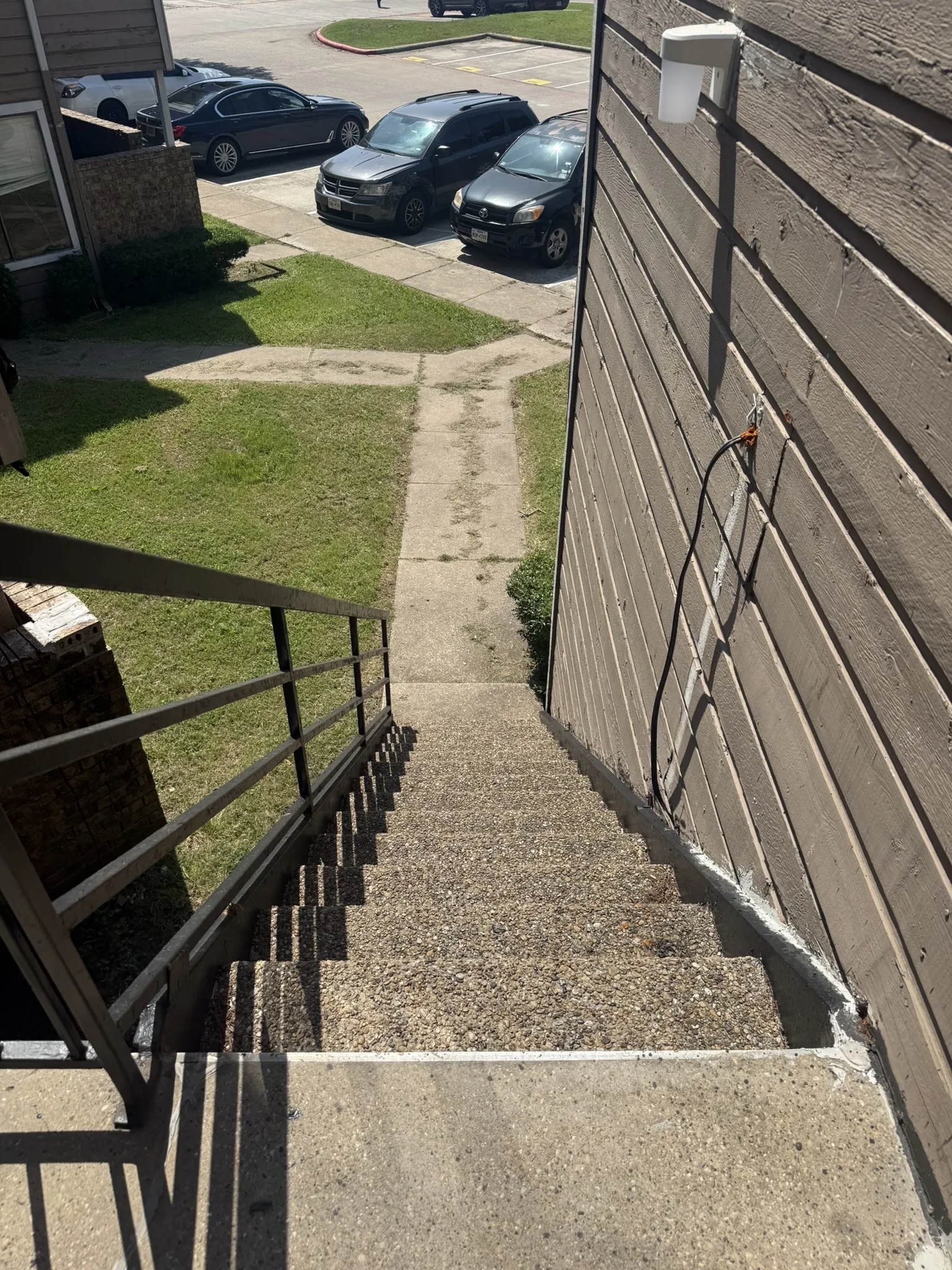 Exterior staircase with textured concrete treads, metal railing, and wall-mounted light fixture