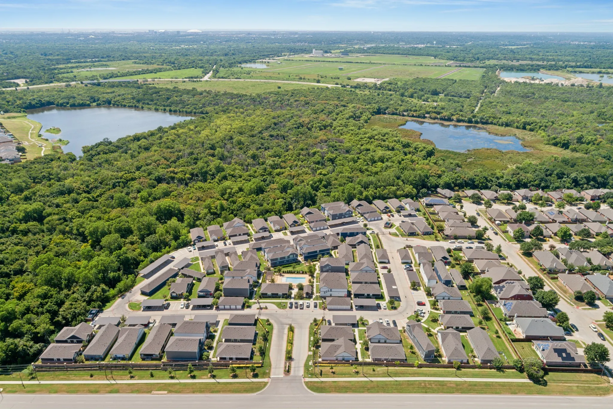 Aerial perspective of a multi-unit residential community featuring a central swimming pool and surrounded by extensive woodland and natural bodies of water