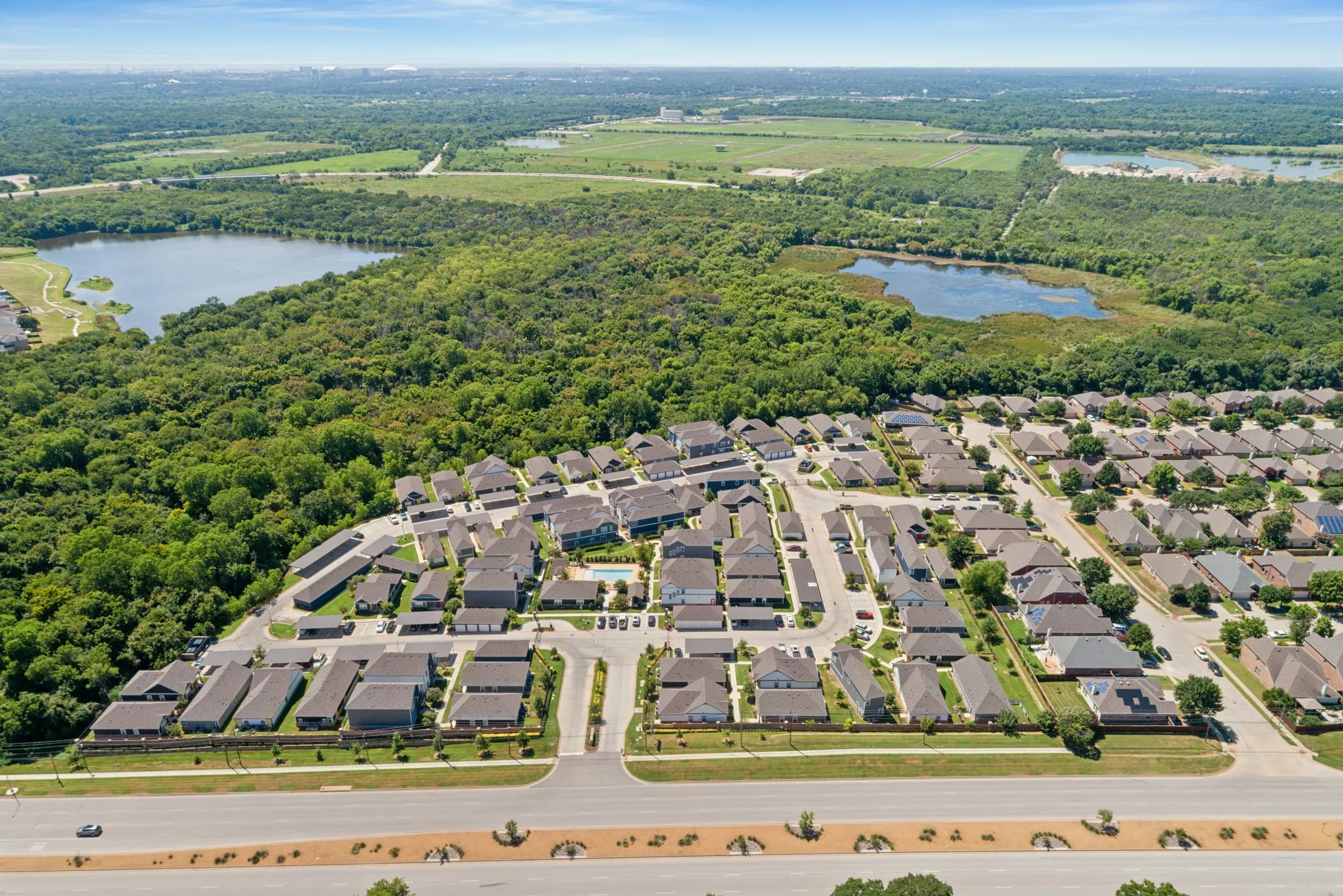 Aerial perspective of residential community featuring a centrally located swimming pool, perimeter forested area, and proximity to natural bodies of water