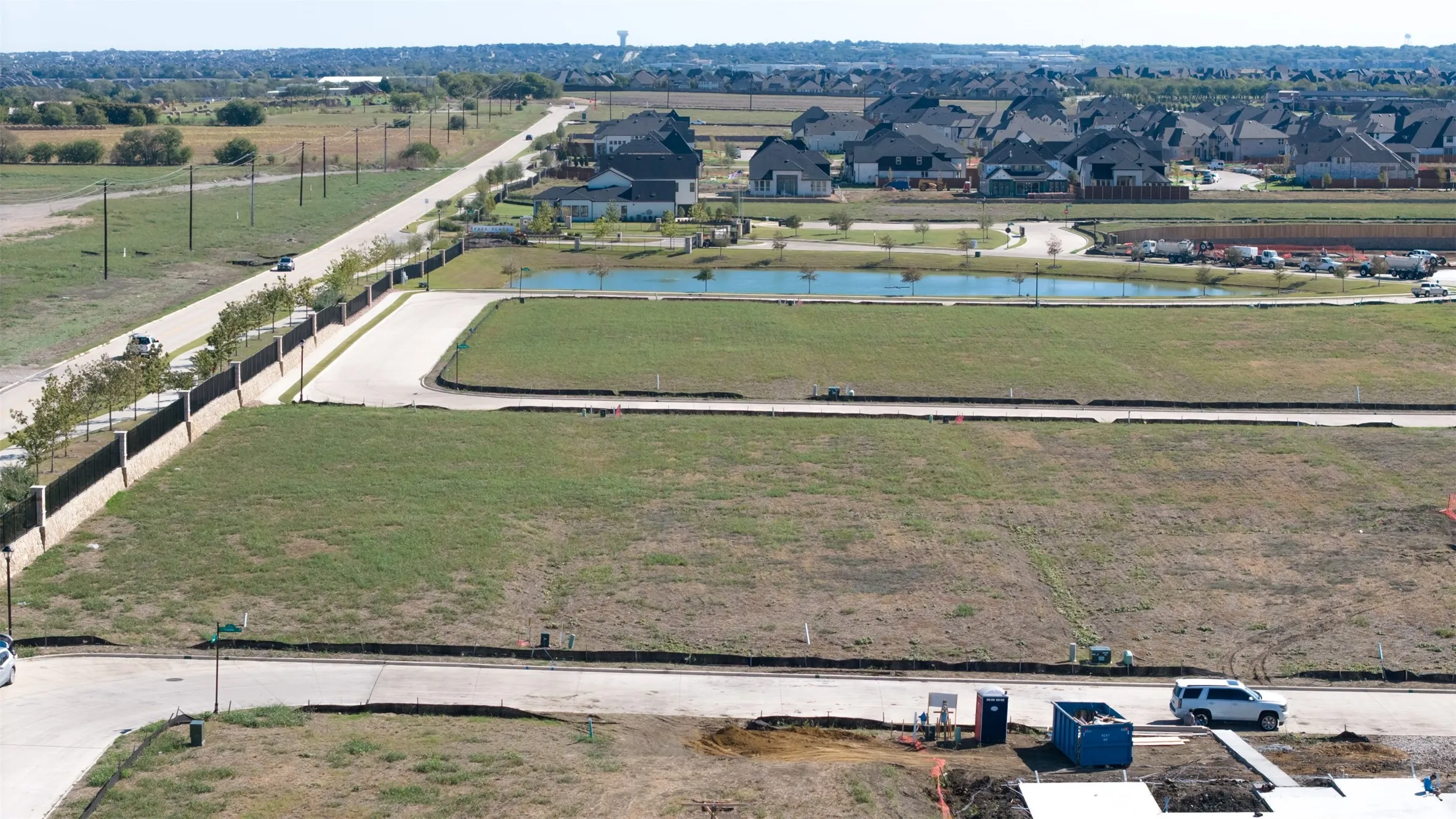 Cleared residential lot featuring street frontage, corner positioning, and perimeter fencing, situated near a retention pond and paved access roads