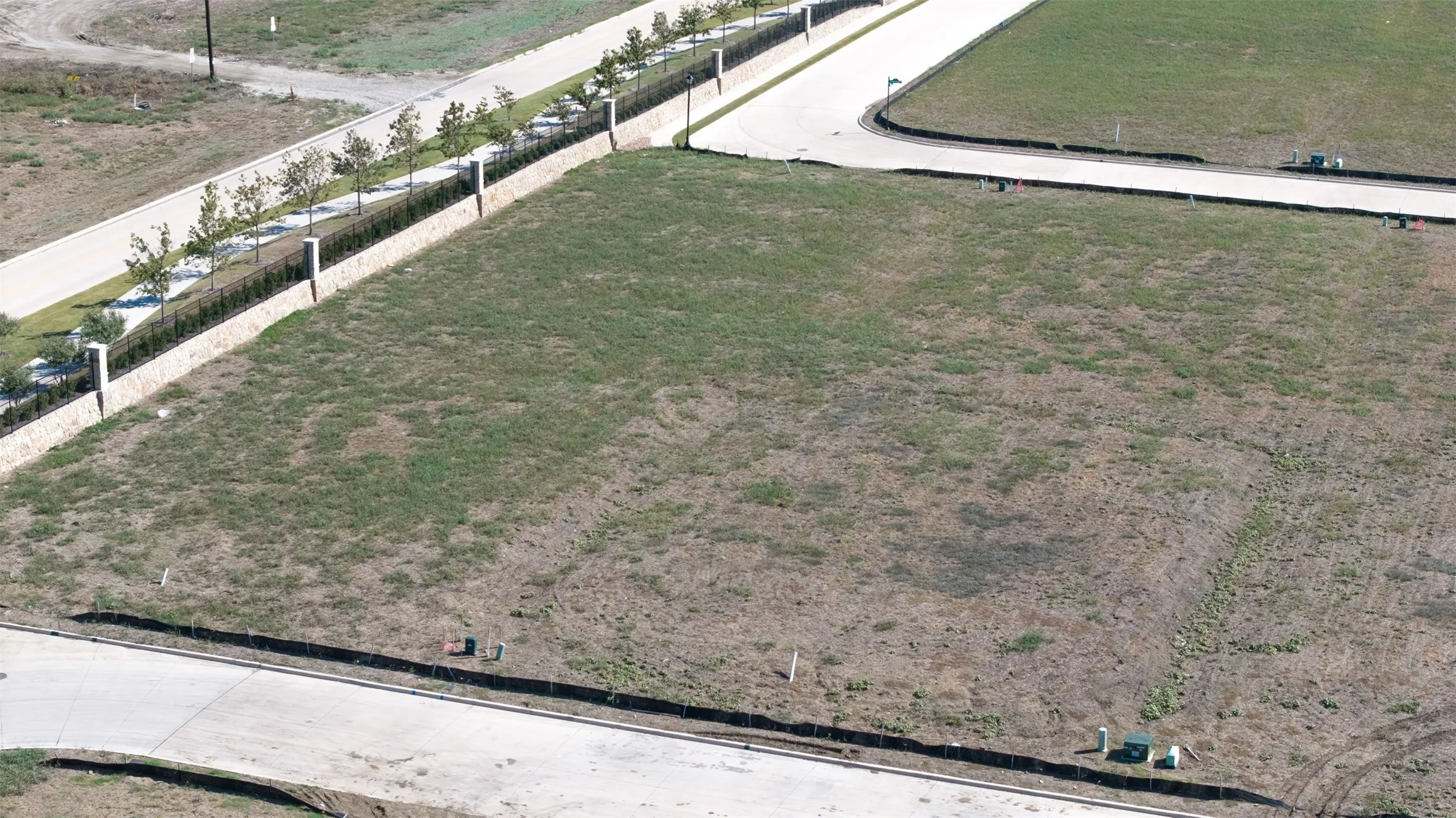 Corner lot featuring concrete street infrastructure, stone perimeter wall, and established landscaping