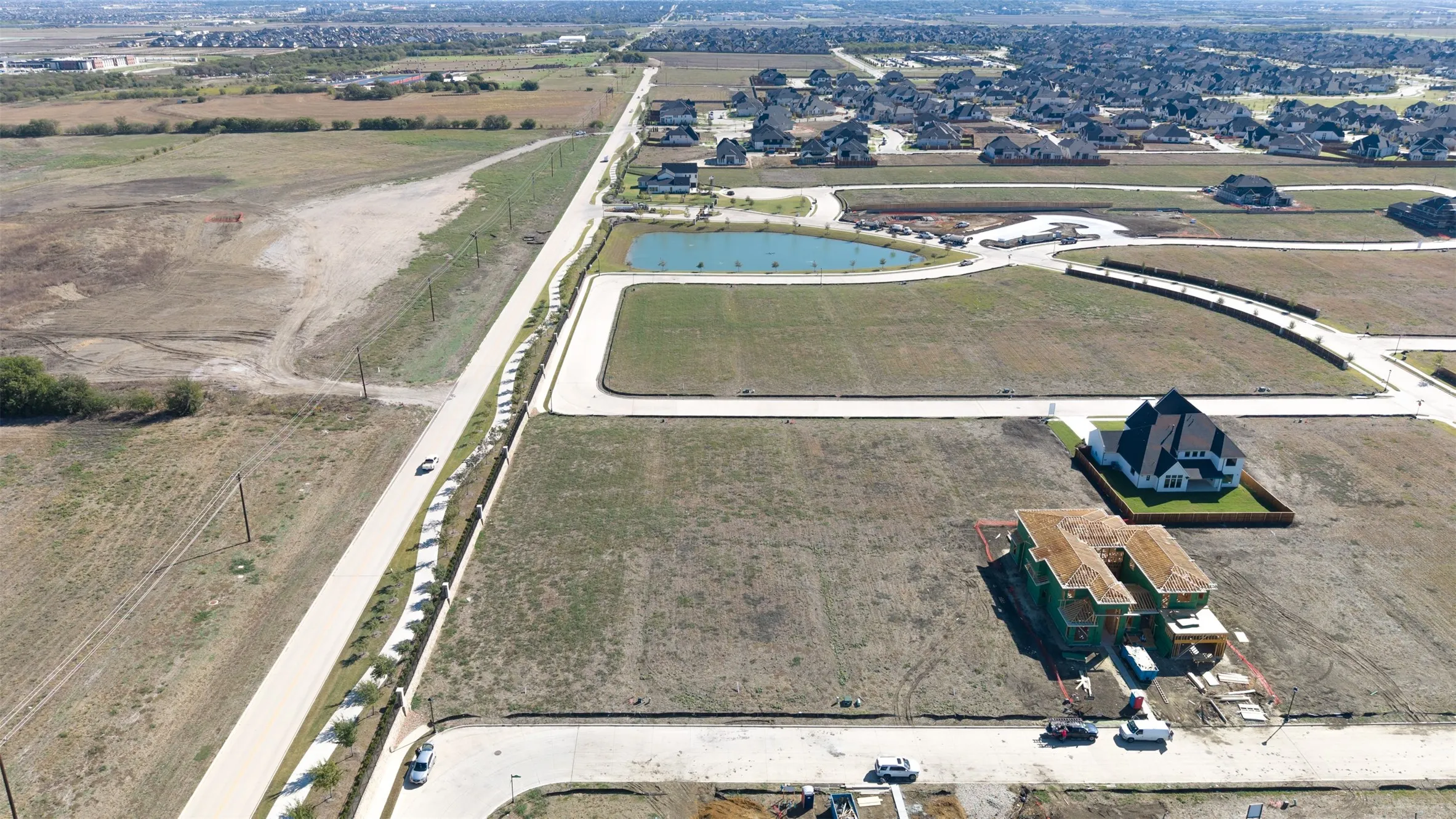 Aerial perspective of a development parcel featuring paved street access, curbing, sidewalk infrastructure, and proximity to a neighborhood pond