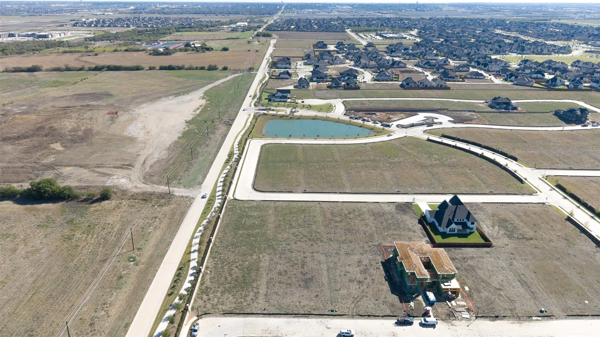 Aerial perspective of expansive residential acreage featuring a paved thoroughfare, proximity to a community pond, and defined land parcels