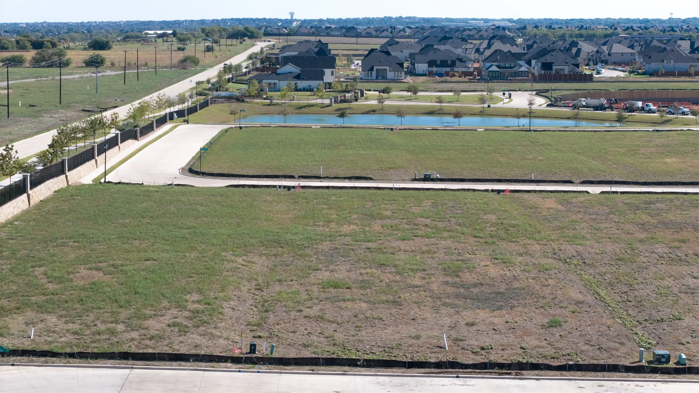 Expansive vacant parcel featuring paved road frontage, leveled terrain, and perimeter drainage fencing