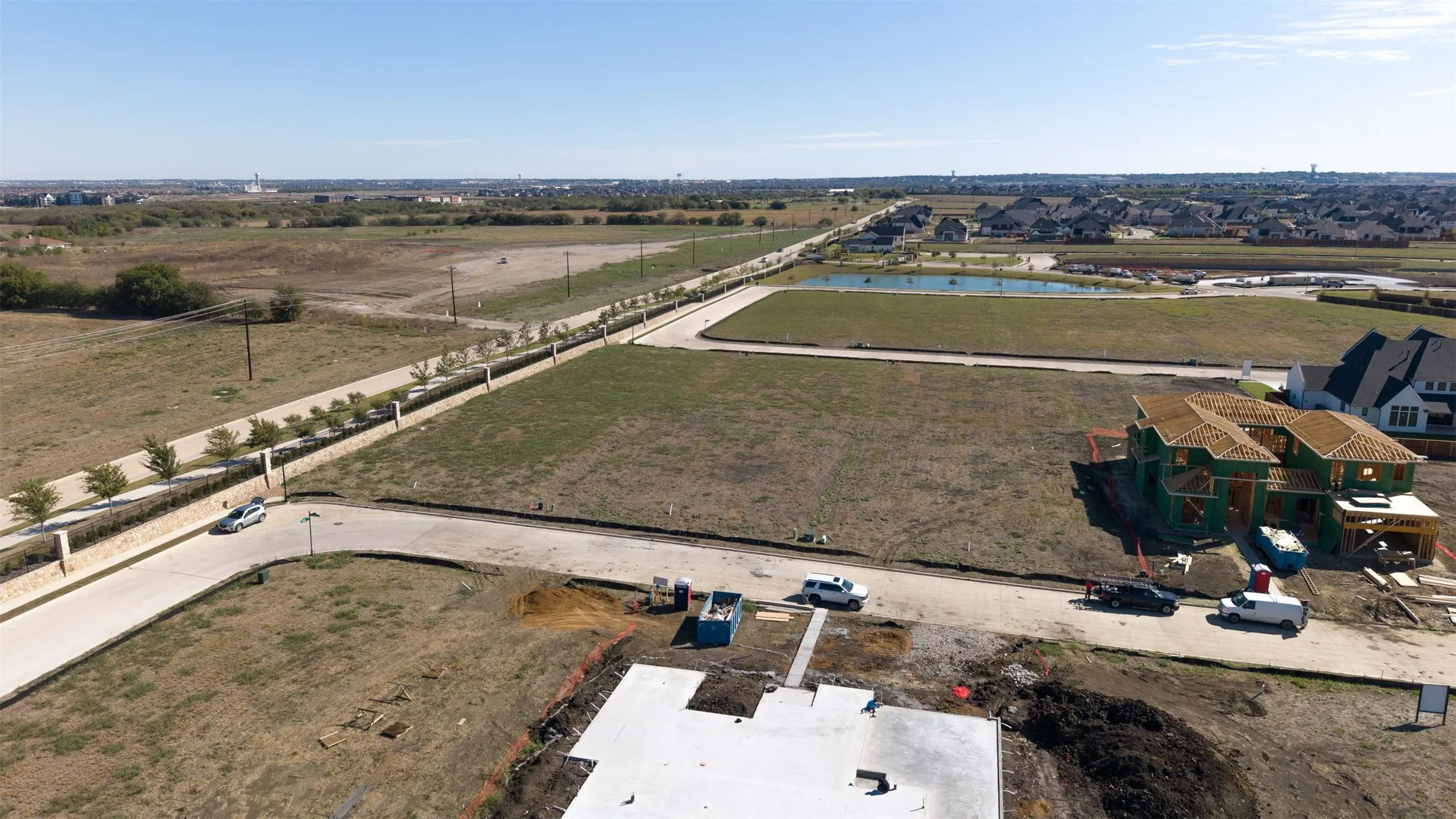 Aerial view of residential development featuring paved concrete streets, established utility infrastructure, perimeter stone fencing, and open lot configurations