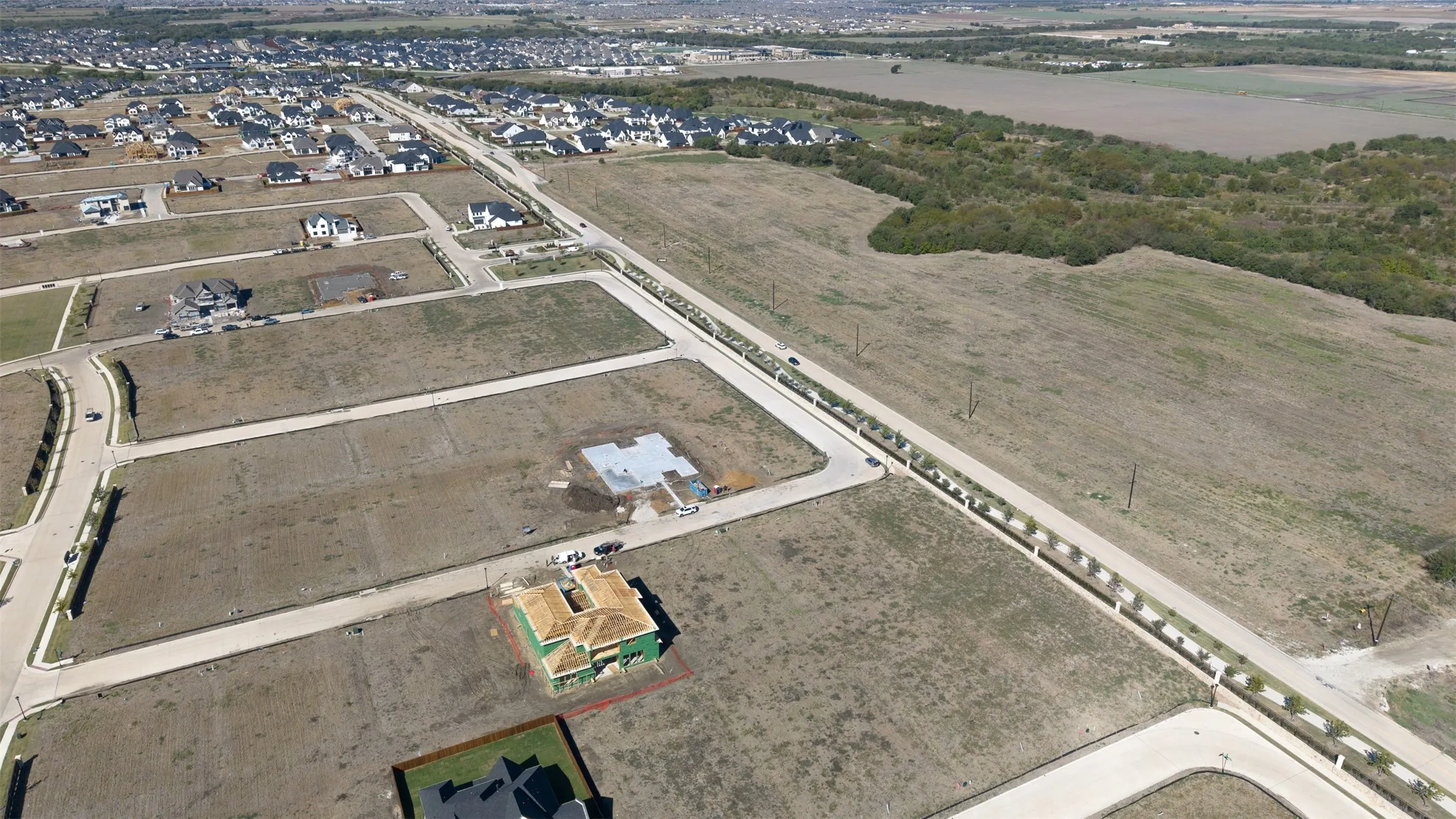 Aerial perspective of a development parcel featuring paved street infrastructure, concrete building foundations, and cleared lots bordered by expansive open space
