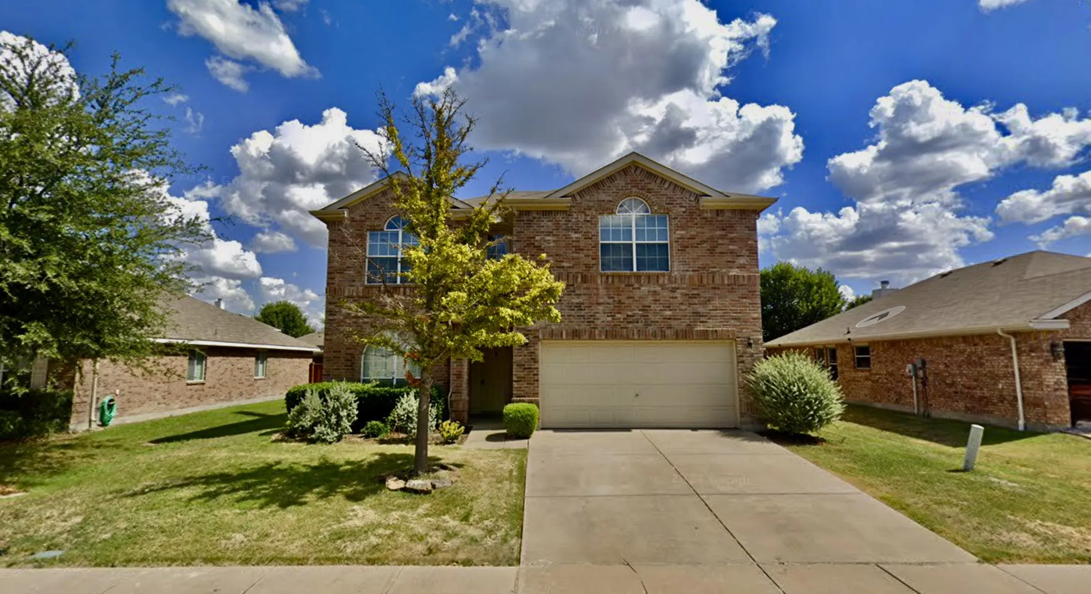 Two-story brick exterior featuring a multi-gabled roofline, arched window detailing, and a concrete driveway leading to an attached two-car garage