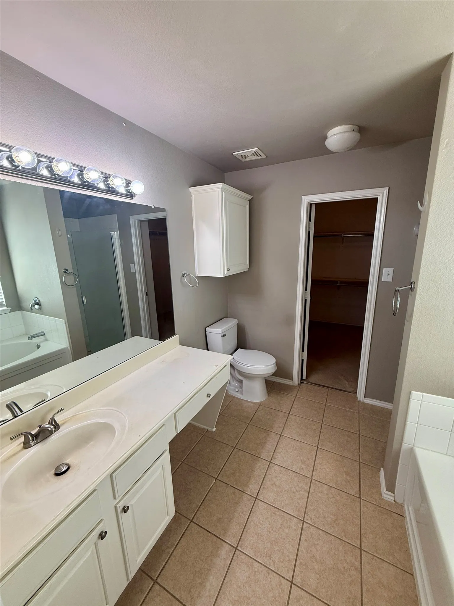 Bathroom featuring a full-width vanity with an integrated sink, white cabinetry, a large wall-mounted mirror with multi-bulb lighting, and tile flooring