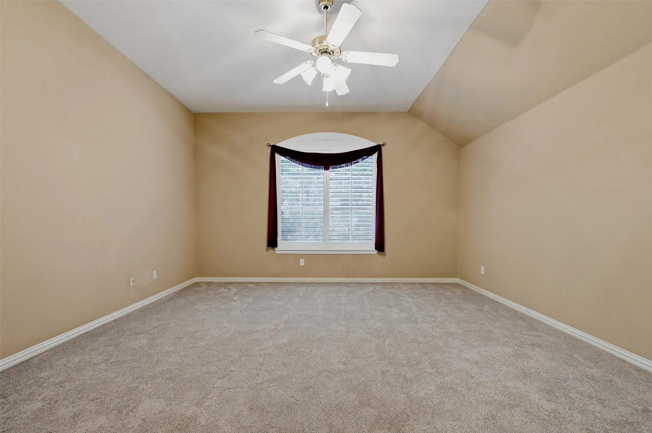 Owner's suite, featuring vaulted ceiling, carpeting, ceiling fan with integrated lighting, and an arched window