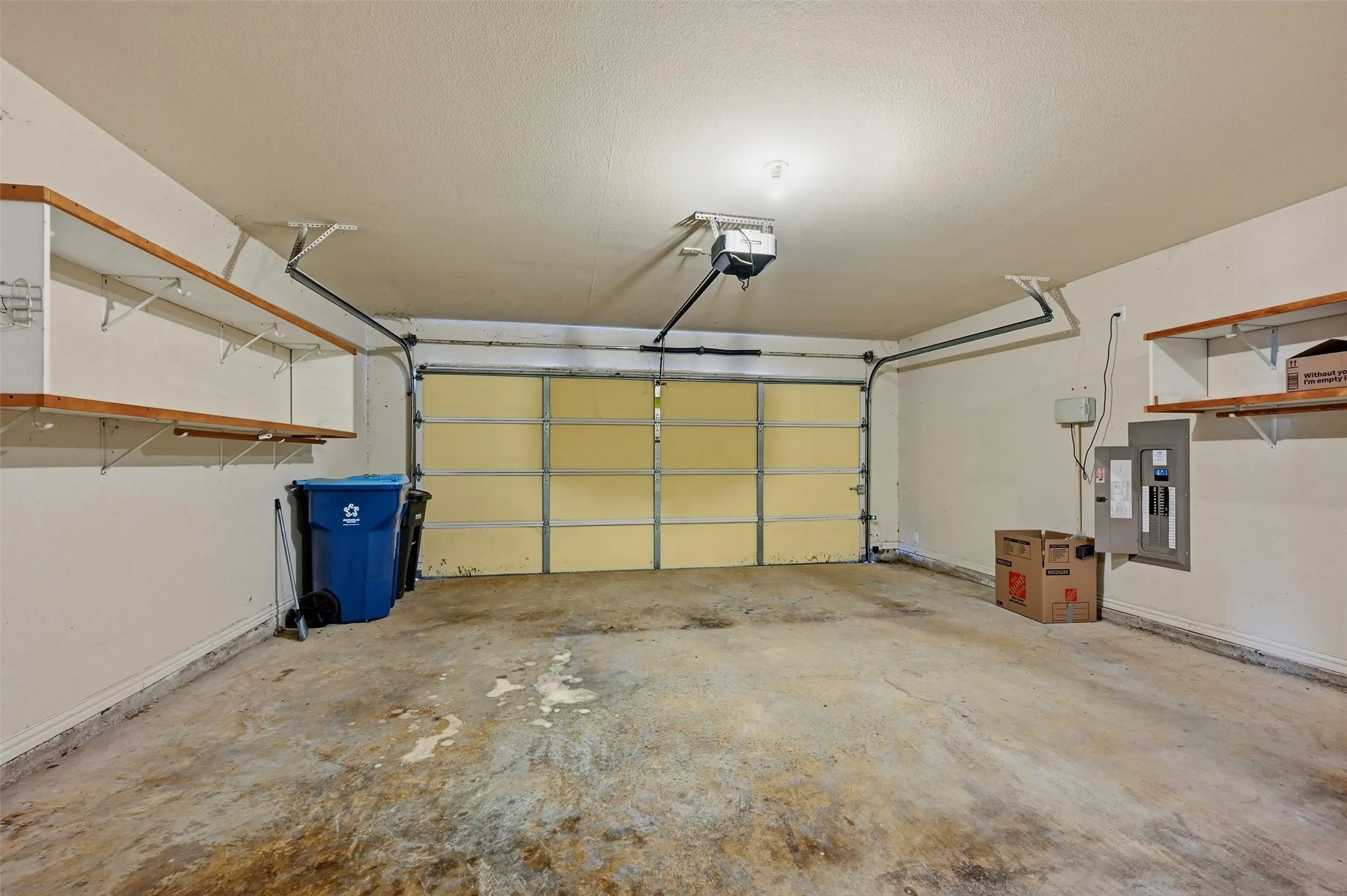 Multi-car garage featuring a concrete floor, built-in wooden shelving, and an integrated overhead door opener