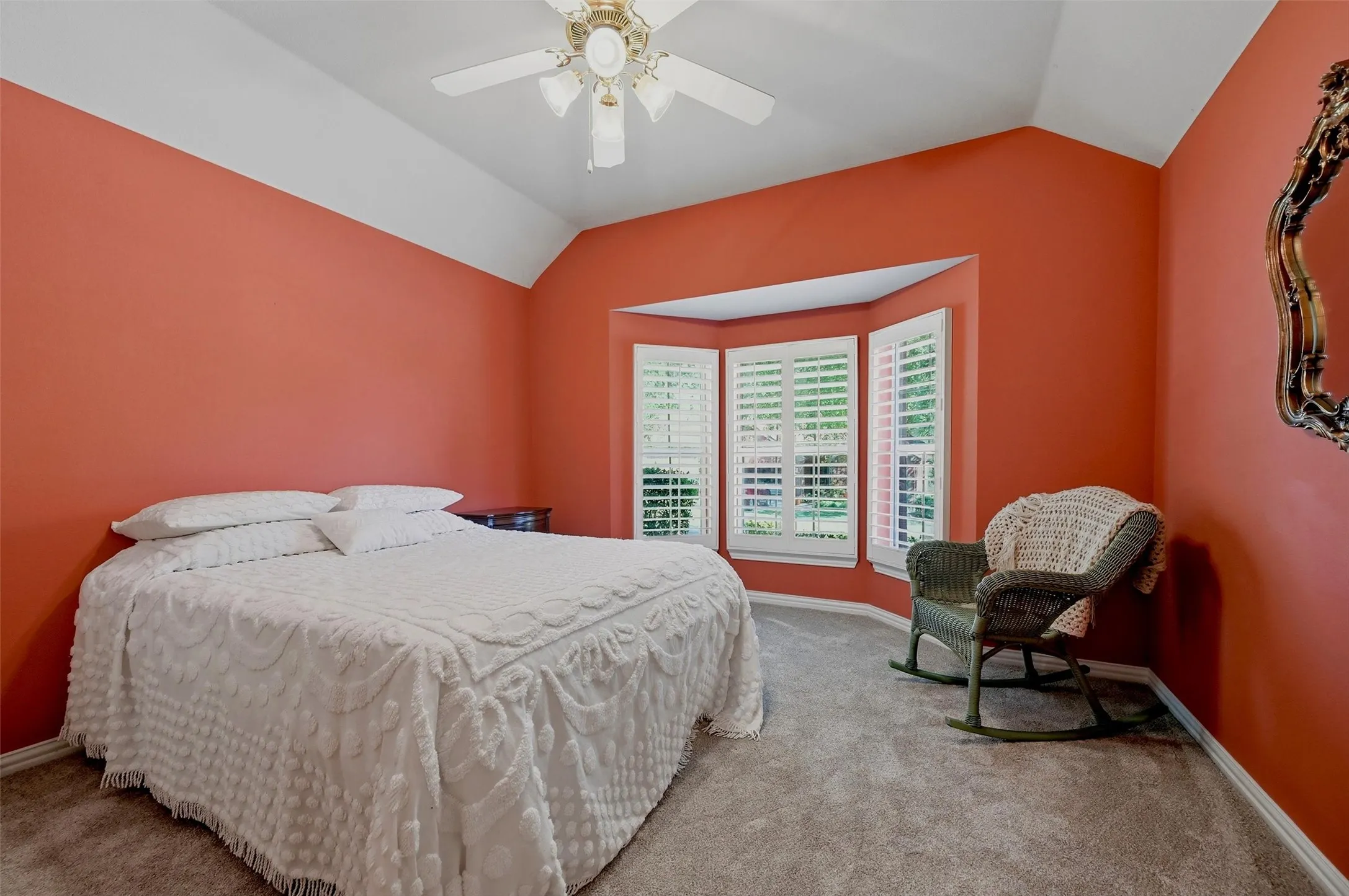 Vaulted ceiling featuring a central lighted ceiling fan, bay window with plantation shutters, and neutral carpeting