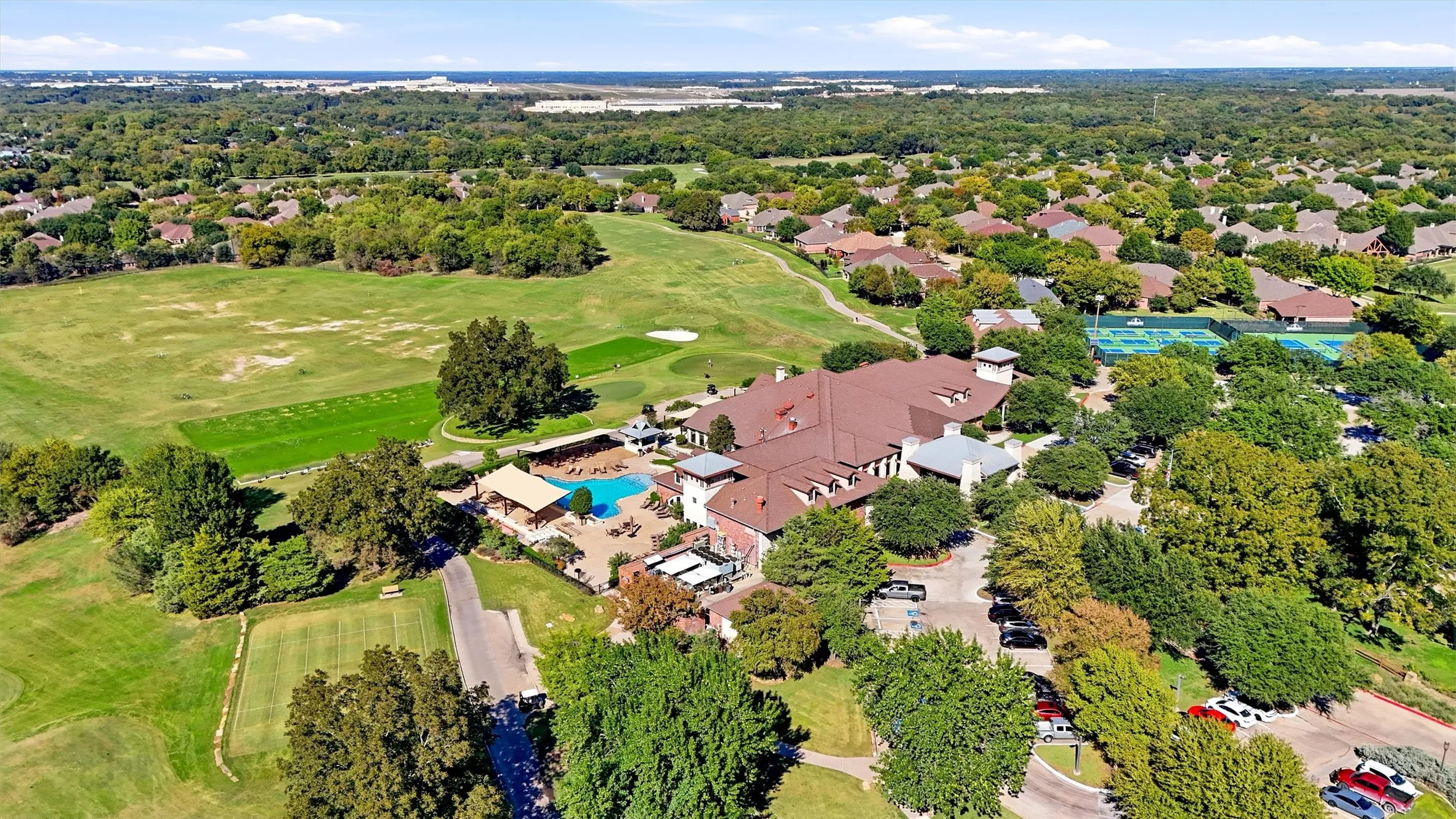 Aerial view featuring an expansive clubhouse, outdoor swimming pool, tennis courts, and bordering golf course greens
