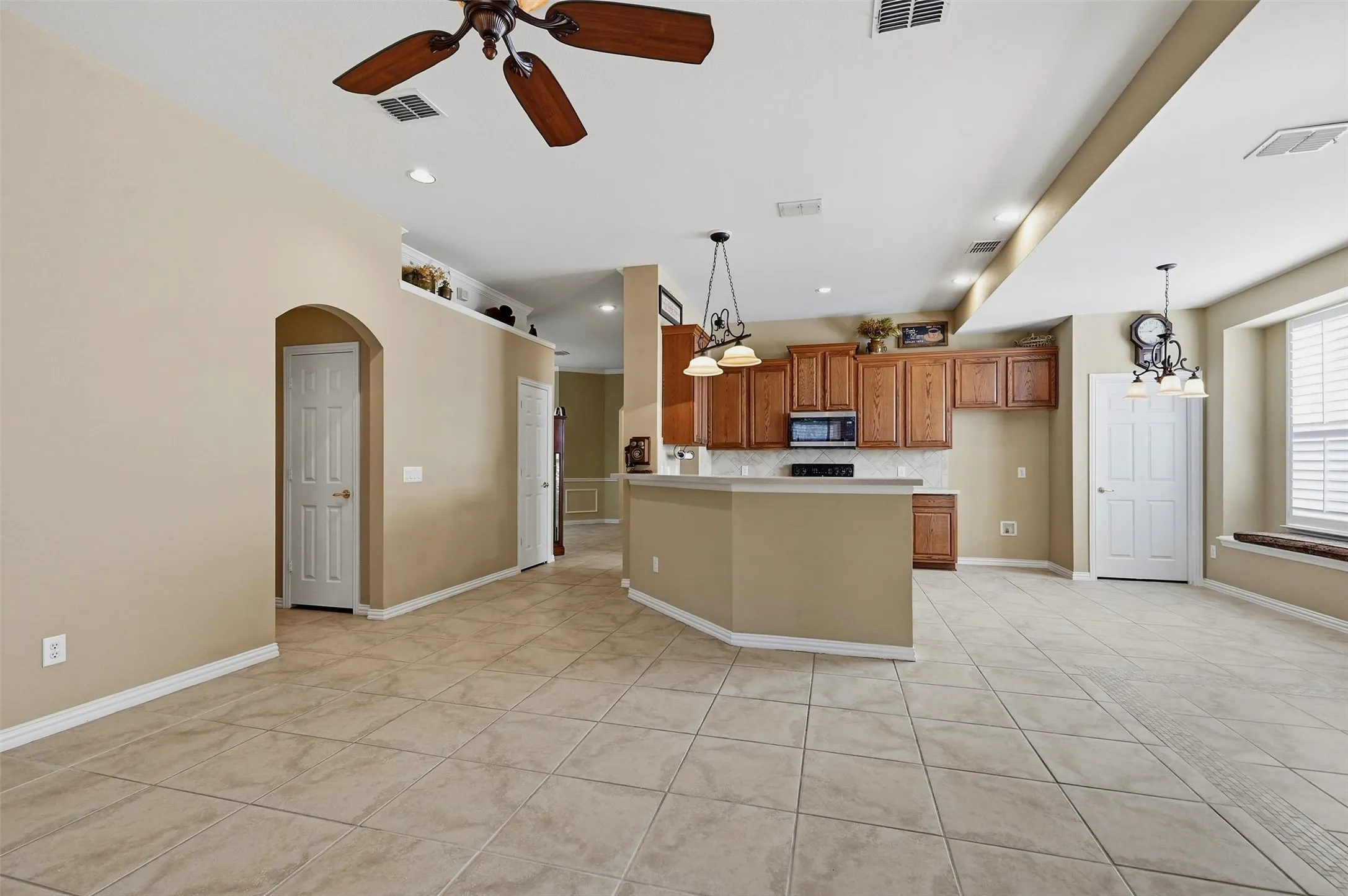 Open-concept interior featuring large-format tile flooring, wood cabinetry, built-in breakfast bar, recessed lighting, and arched doorway entry