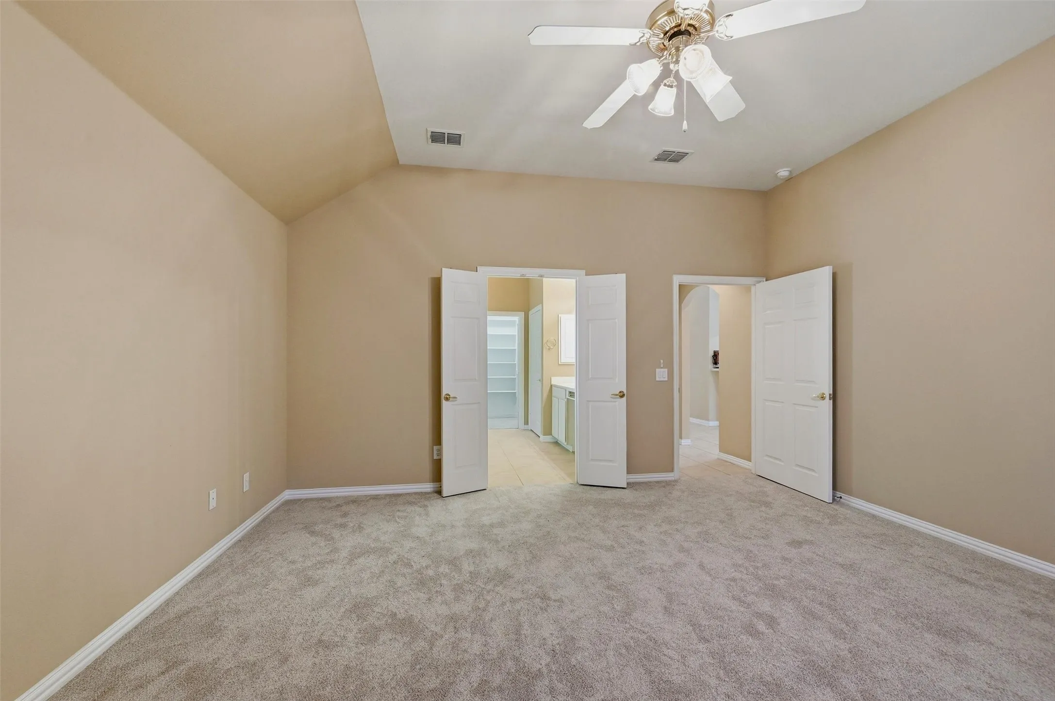 Vaulted ceiling room featuring neutral carpeting, a multi-light ceiling fan, and double-panel entry doors