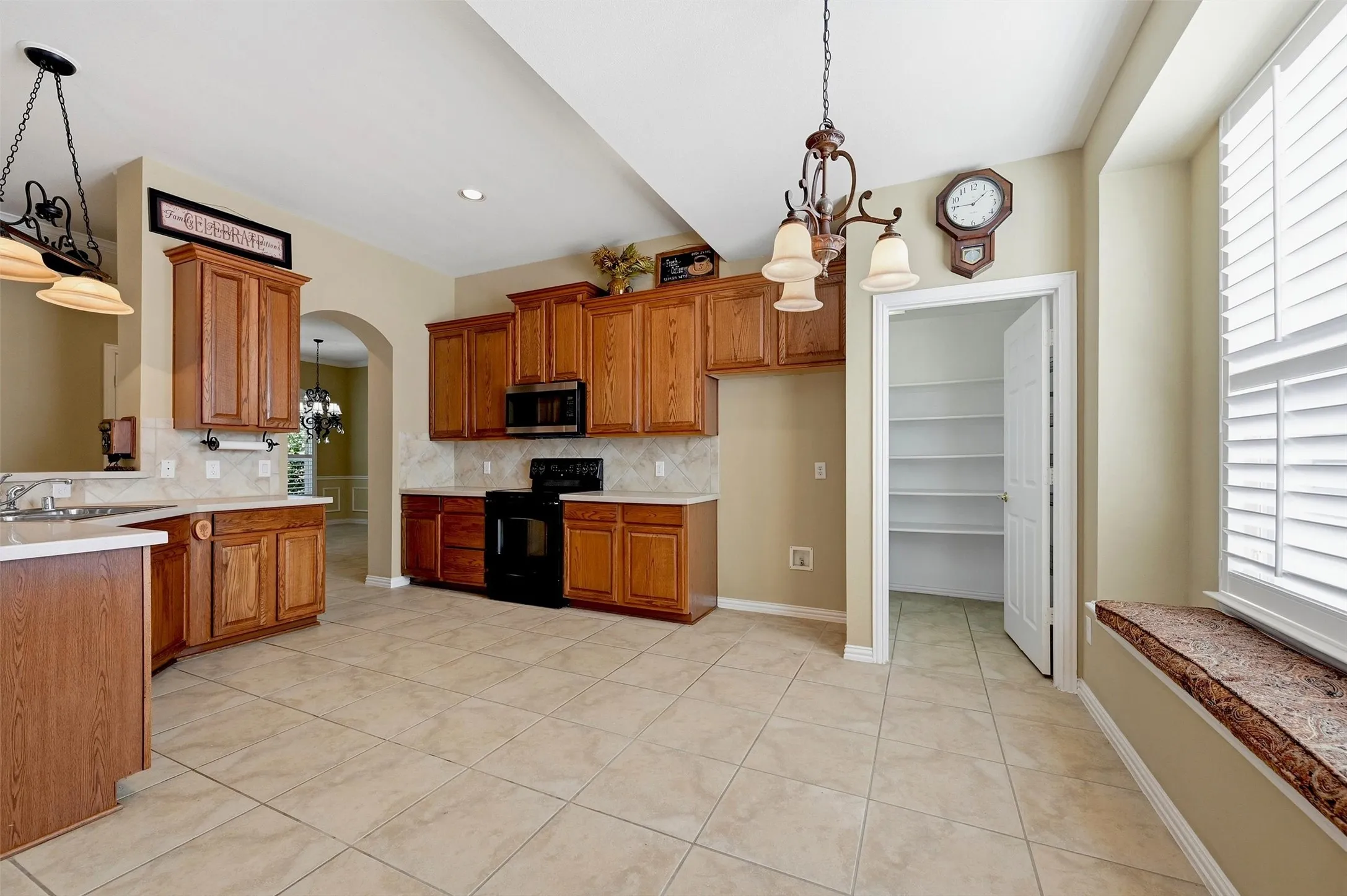 Kitchen featuring wood cabinetry, tile flooring, built-in pantry with shelving, solid surface countertops, and a window seat with plantation shutters
