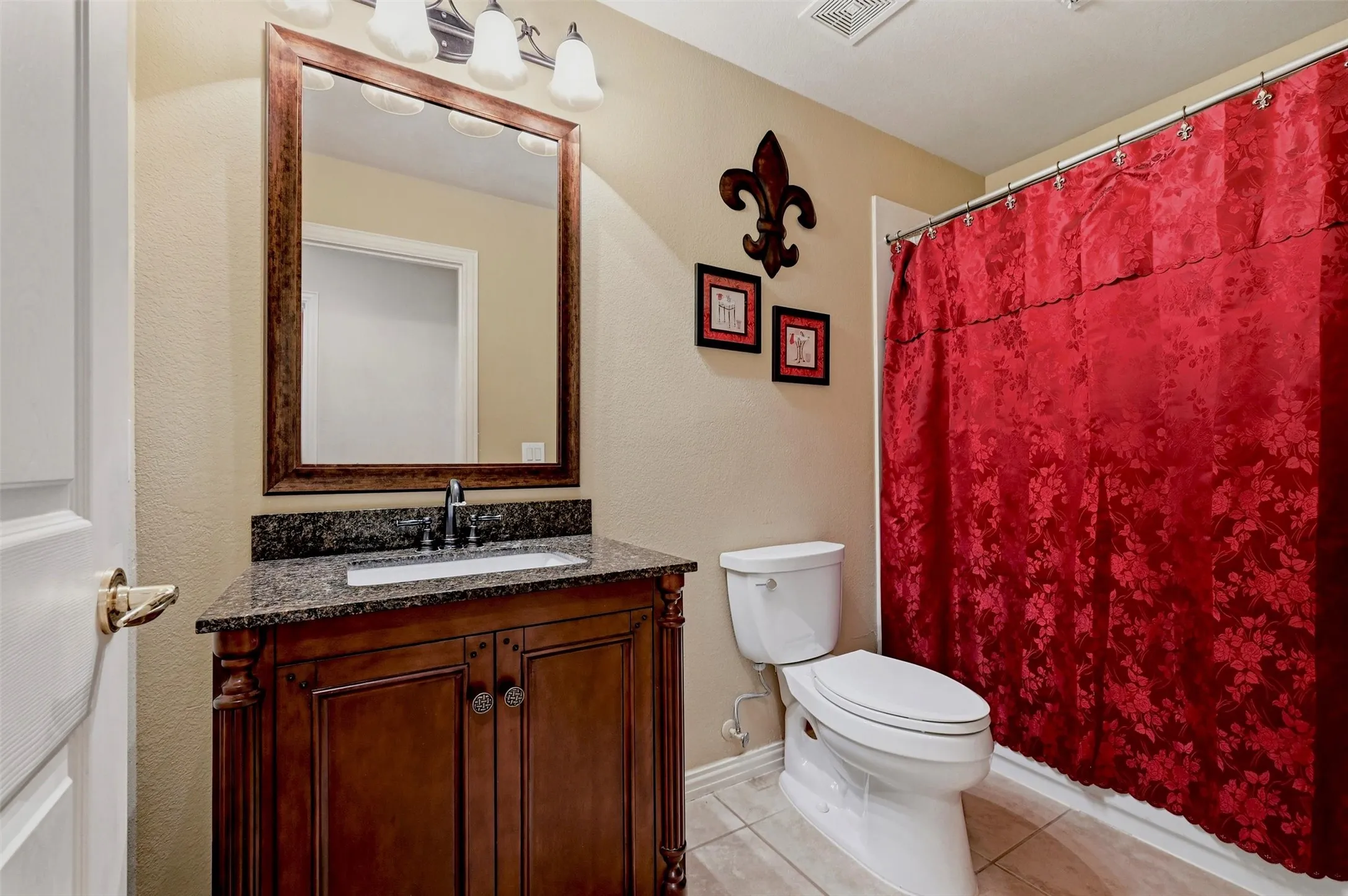 Bathroom featuring a wooden vanity, stone countertop, undermount sink, matching framed mirror, and tiled flooring