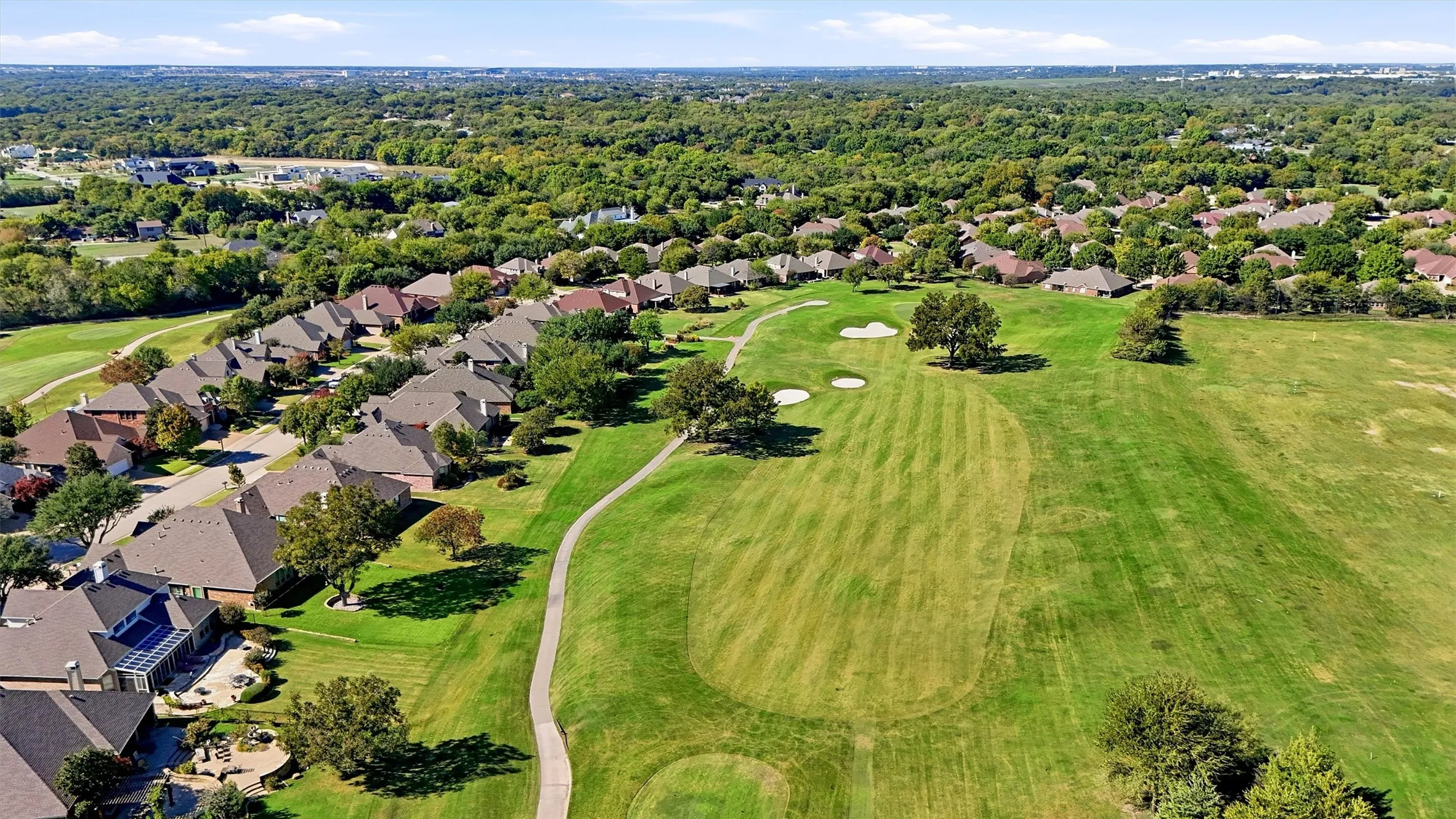 Aerial perspective of a residential community featuring expansive manicured greens, sand bunkers, mature landscaping, and concrete pathways