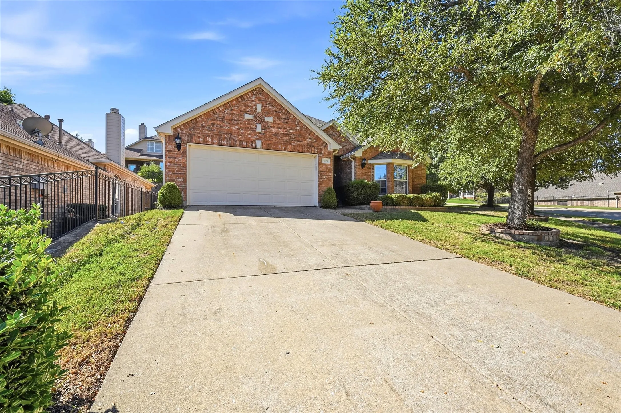 Brick exterior with gable roofline, two-car garage, concrete driveway, and mature landscaping