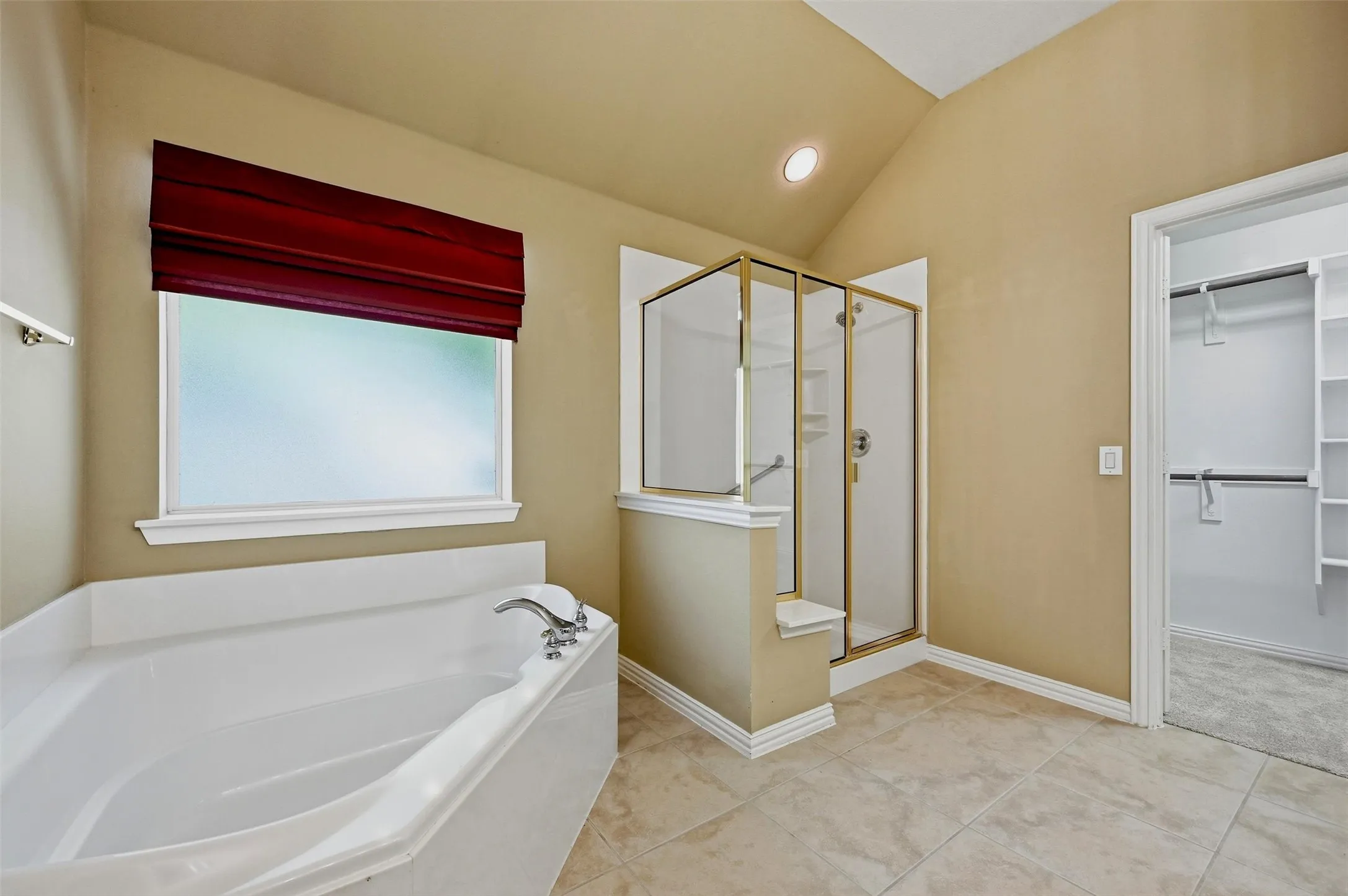 Bathroom featuring a white soaking tub, a separate glass-enclosed shower with gold-tone framing, tile flooring, and a walk-in closet with built-in shelving