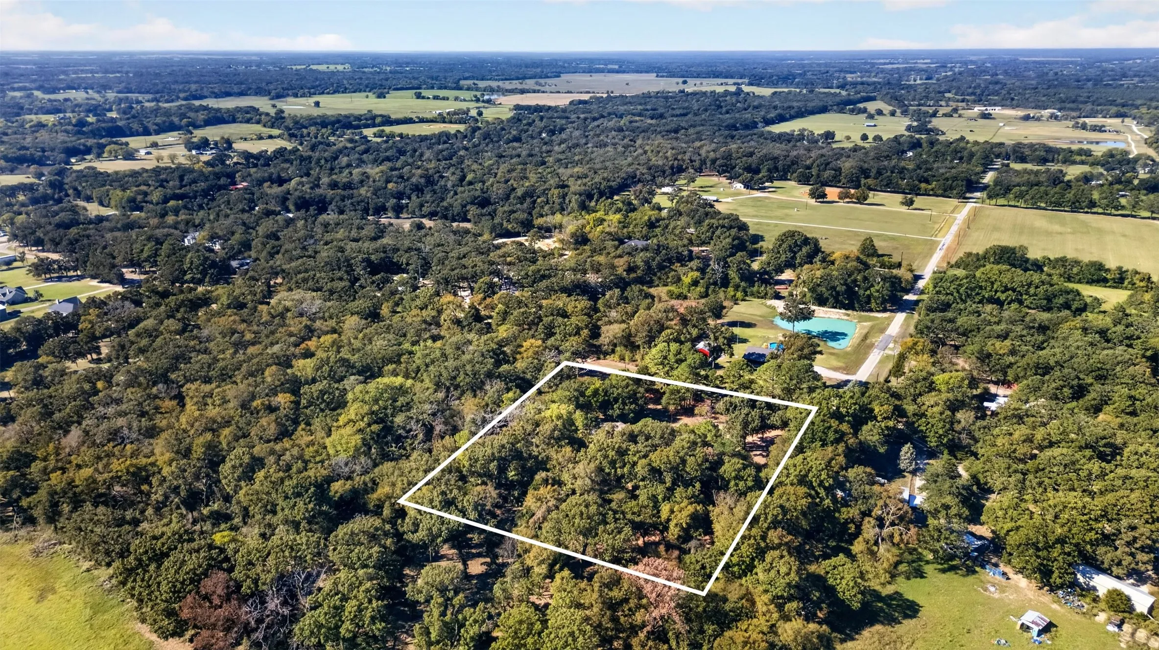 Aerial perspective featuring a heavily wooded parcel of land with mature trees and direct frontage on a paved road