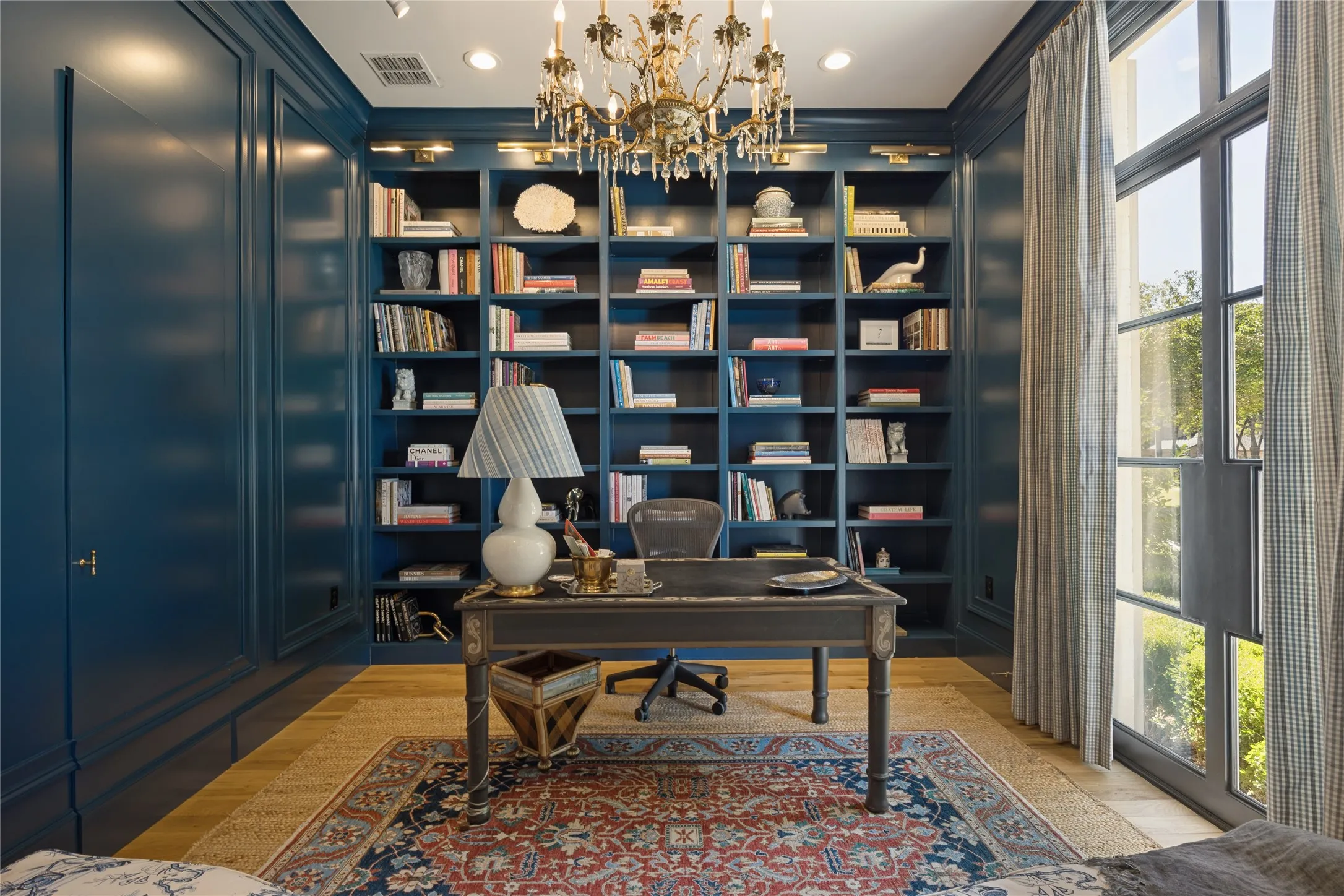 Custom floor-to-ceiling built-in cabinetry, wood-finish flooring, ornate multi-arm chandelier, recessed lighting, and metal-framed glass doors