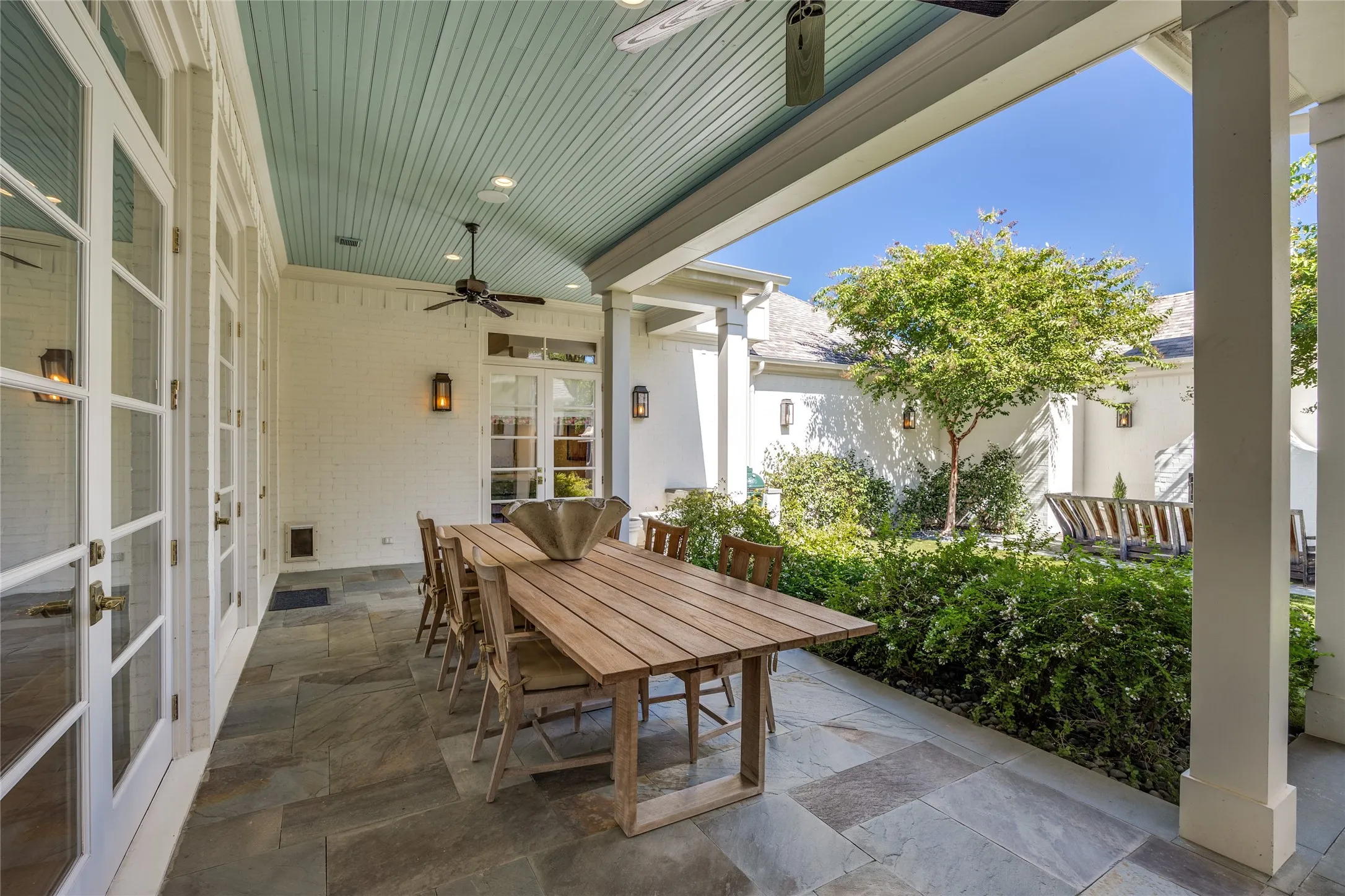 Covered patio featuring stone tile flooring, painted beadboard ceiling, white brick exterior walls, and multiple sets of glass-paned French doors