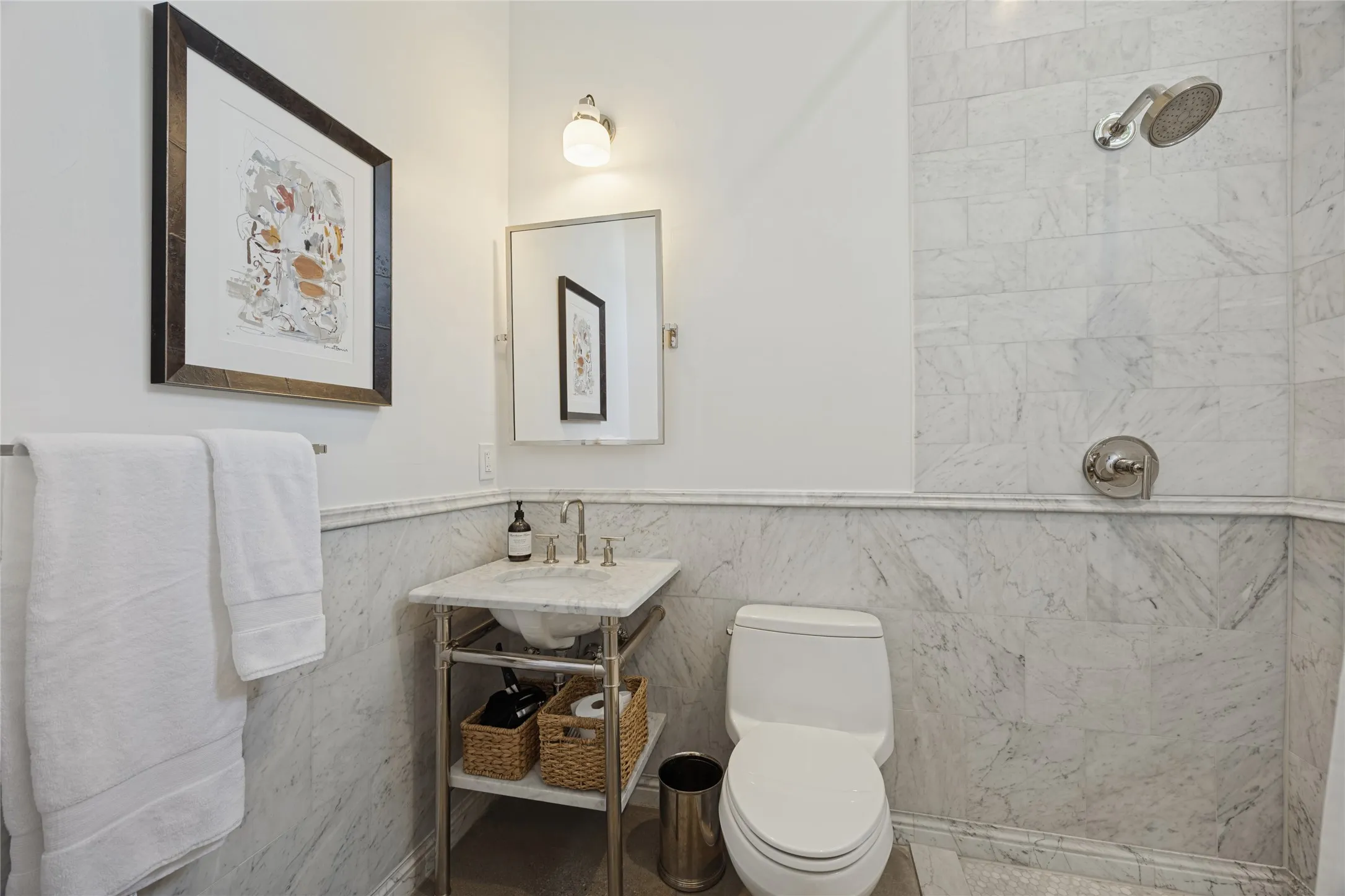 Stone-tiled walls with coordinating chair rail, metal-frame console vanity with stone countertop, wall-mounted light fixture, and fixed shower head.  This bathroom is located in the attached, private guest residence.