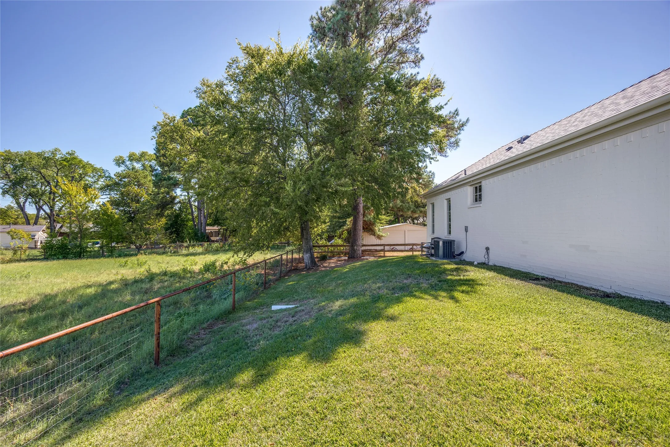Expansive backyard featuring a fenced perimeter, established trees, and a painted brick exterior