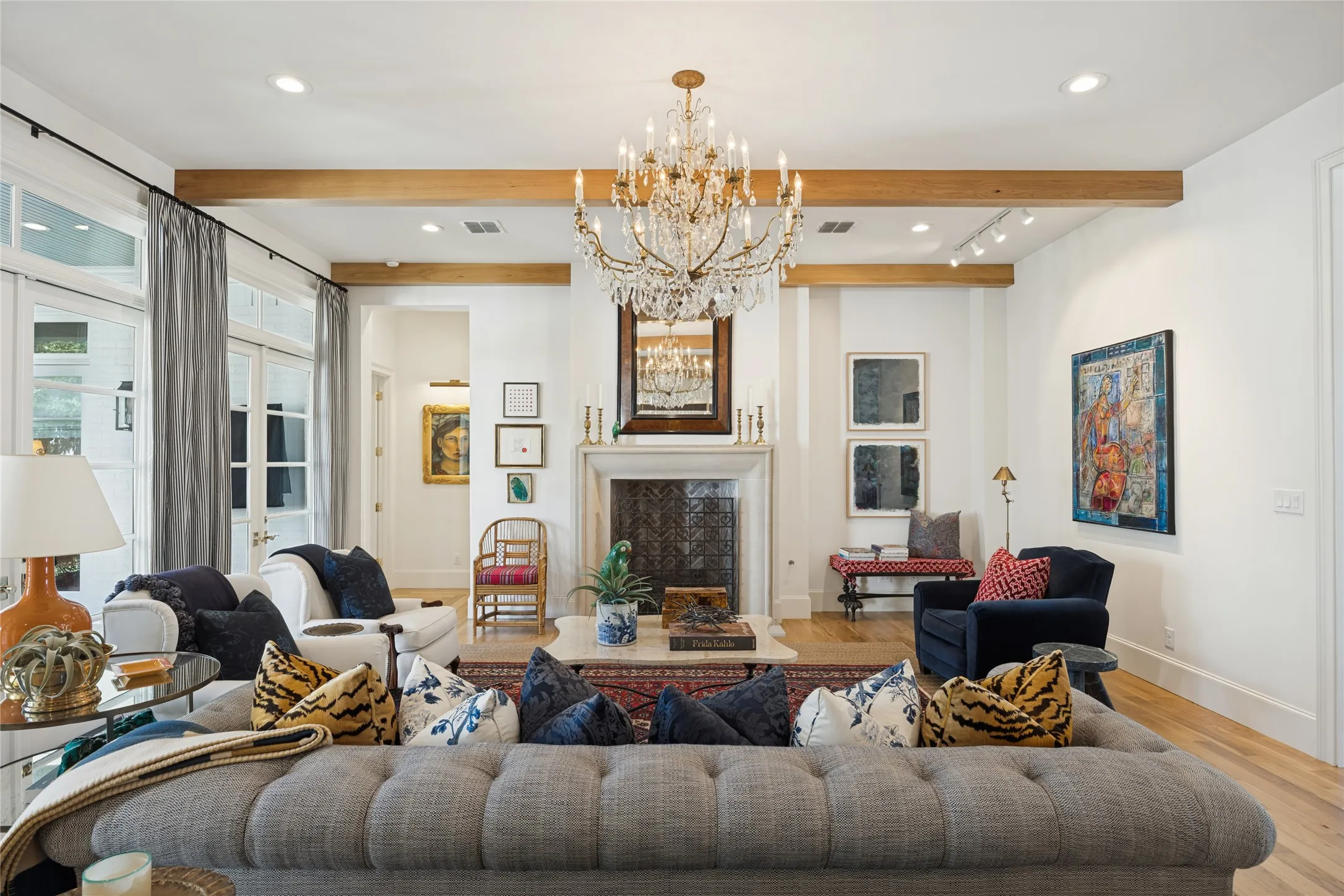 Living area featuring wood ceiling beams, a stone-surround fireplace with a patterned firebox, crystal chandelier, recessed lighting, and wood-finish flooring