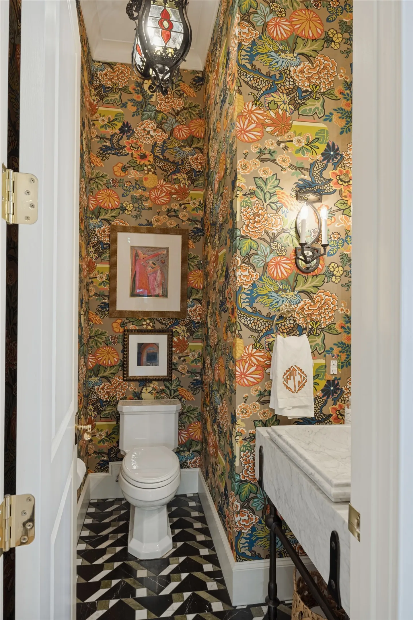 Powder room featuring decorative floral wallpaper, geometric patterned stone tile flooring, a wall-mounted stone vanity with a metal base, a multi-tiered hanging lantern, and a dual-armed wall sconce