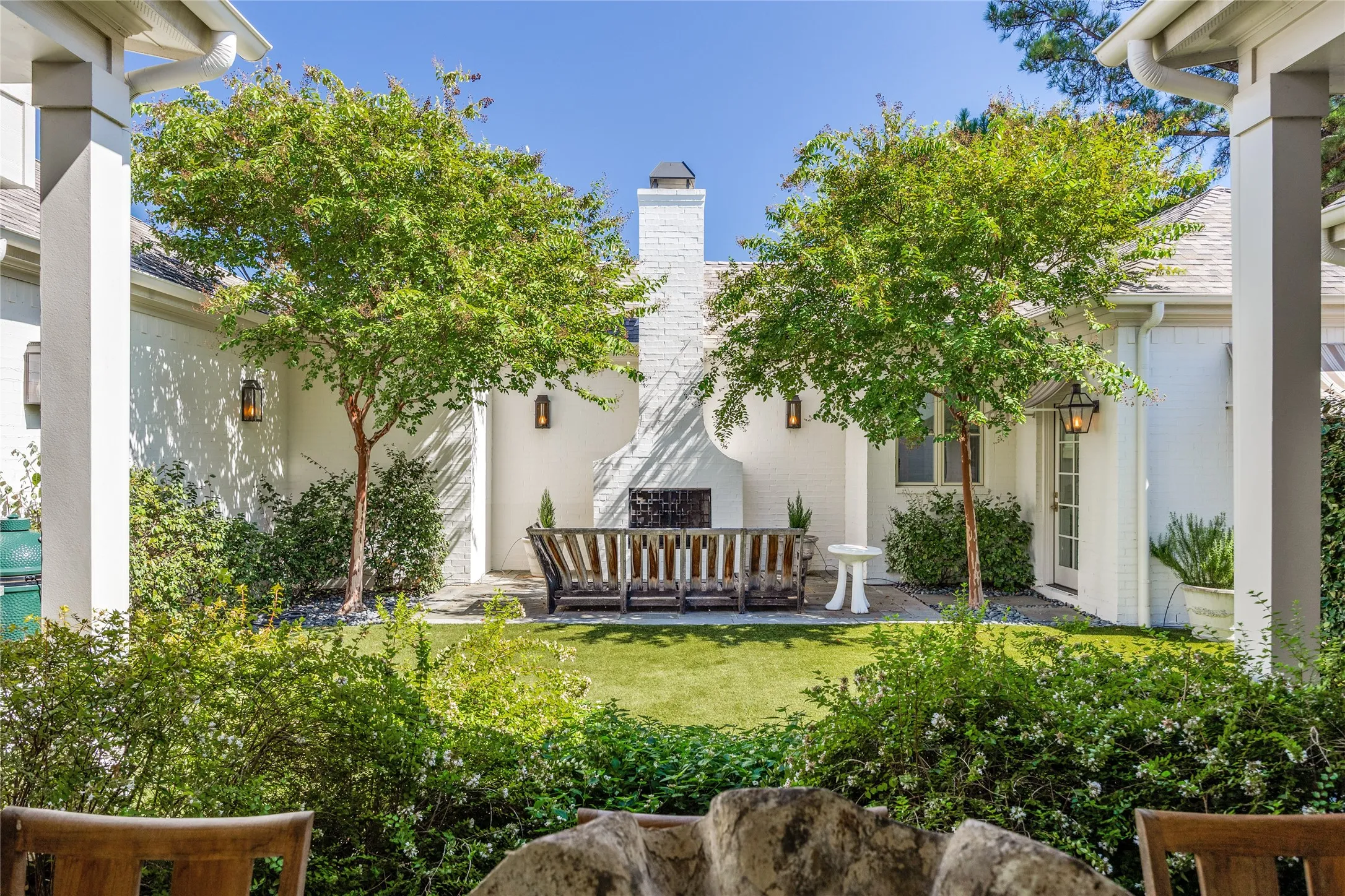 Enclosed courtyard featuring a painted brick exterior, stone flooring, a central masonry fireplace, and landscaped plantings