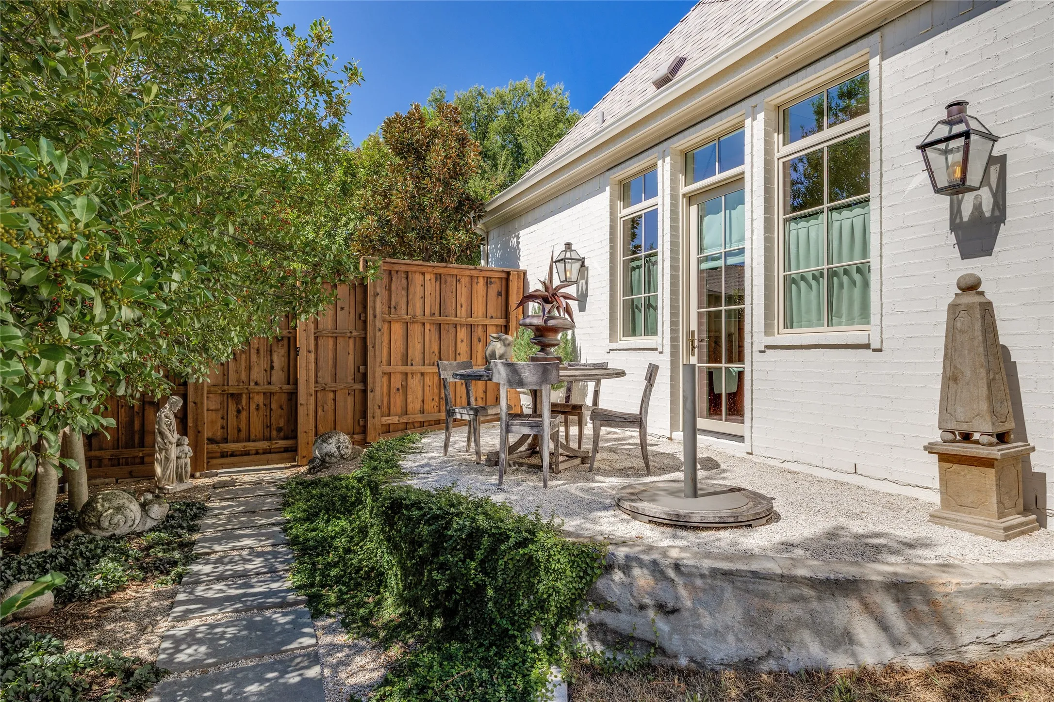 Painted brick exterior featuring a white facade, gravel patio, stone retaining wall, slate walkway, and wood-finish privacy fencing