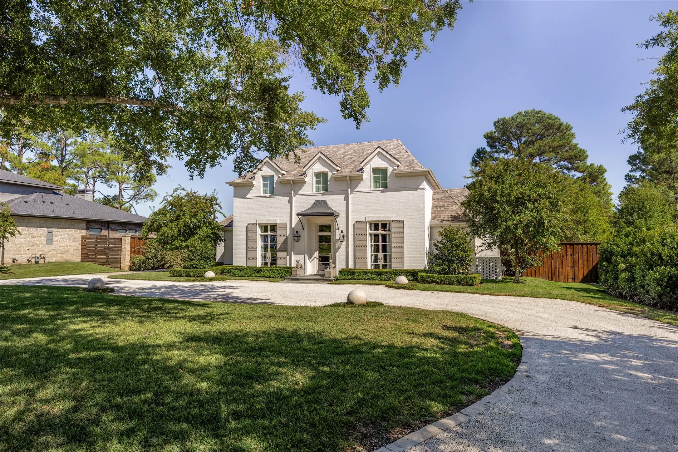 Traditional painted brick exterior featuring dormer windows, a custom metal entryway awning, arched window treatments, and a gravel motor court