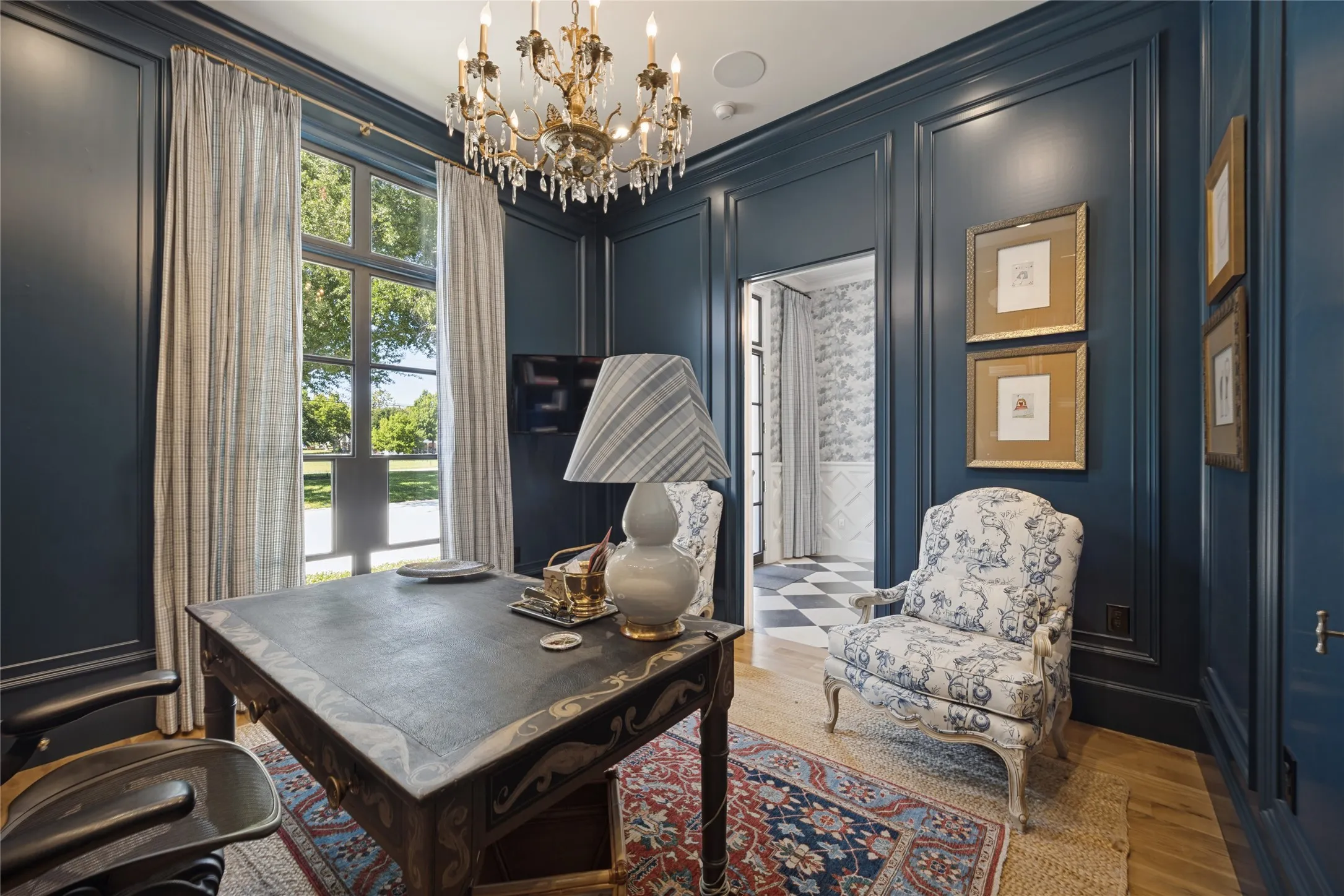 Room featuring floor-to-ceiling wainscoting, intricate crown molding, dark-toned wall paneling, a multi-tier crystal chandelier, and a large multi-pane window with wooden-finish flooring
