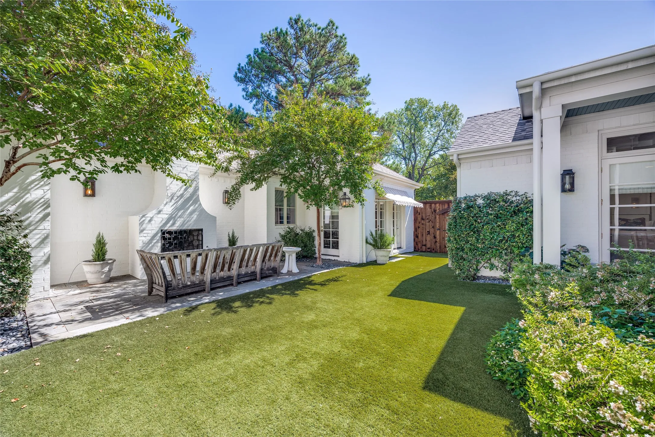 Exterior courtyard featuring a painted brick finish, an integrated outdoor fireplace, synthetic turf, and wall-mounted exterior lighting