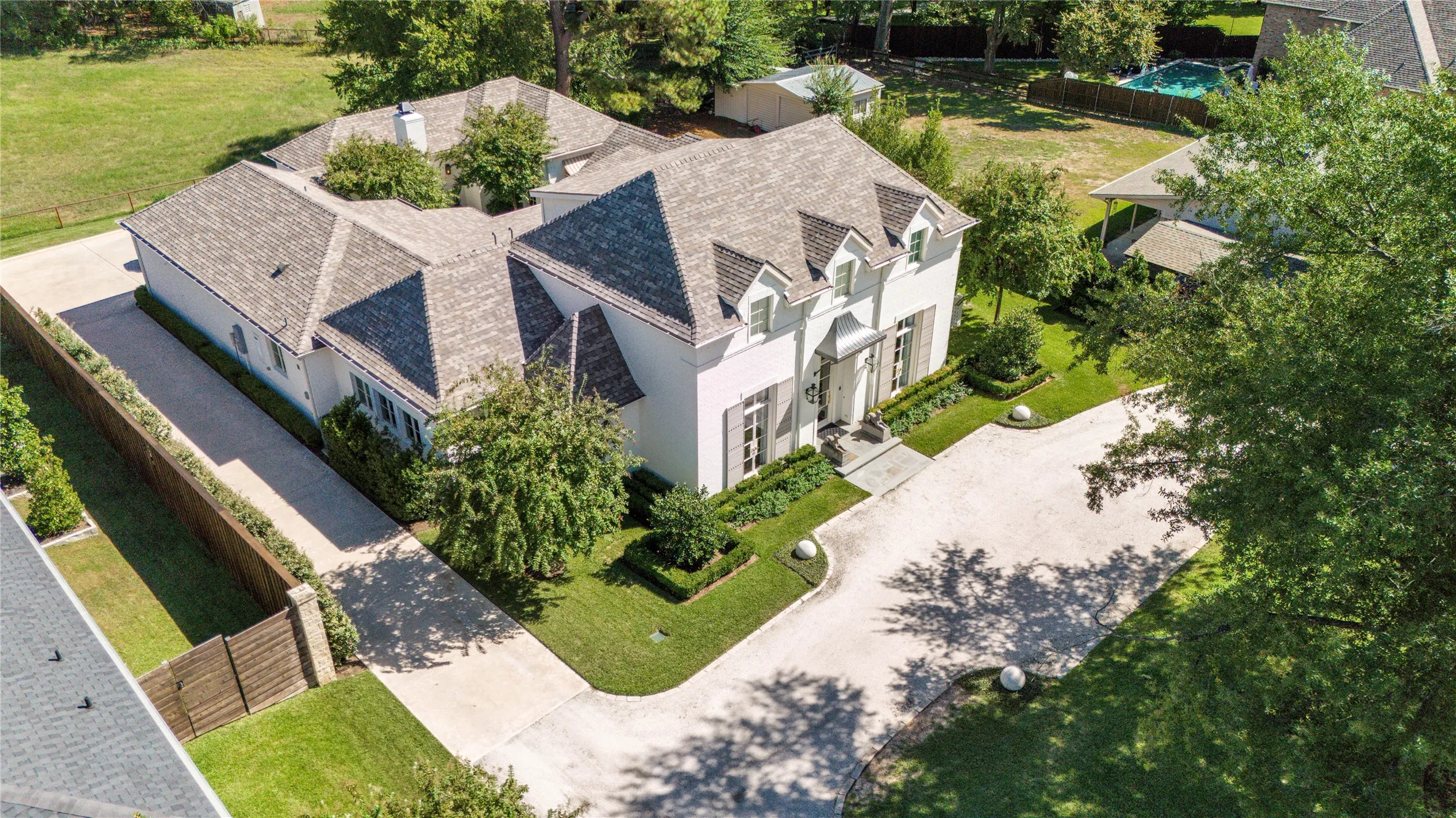 Multi-gabled light-toned exterior featuring a expansive concrete motor court, professional landscaping, and extensive tree-lined grounds