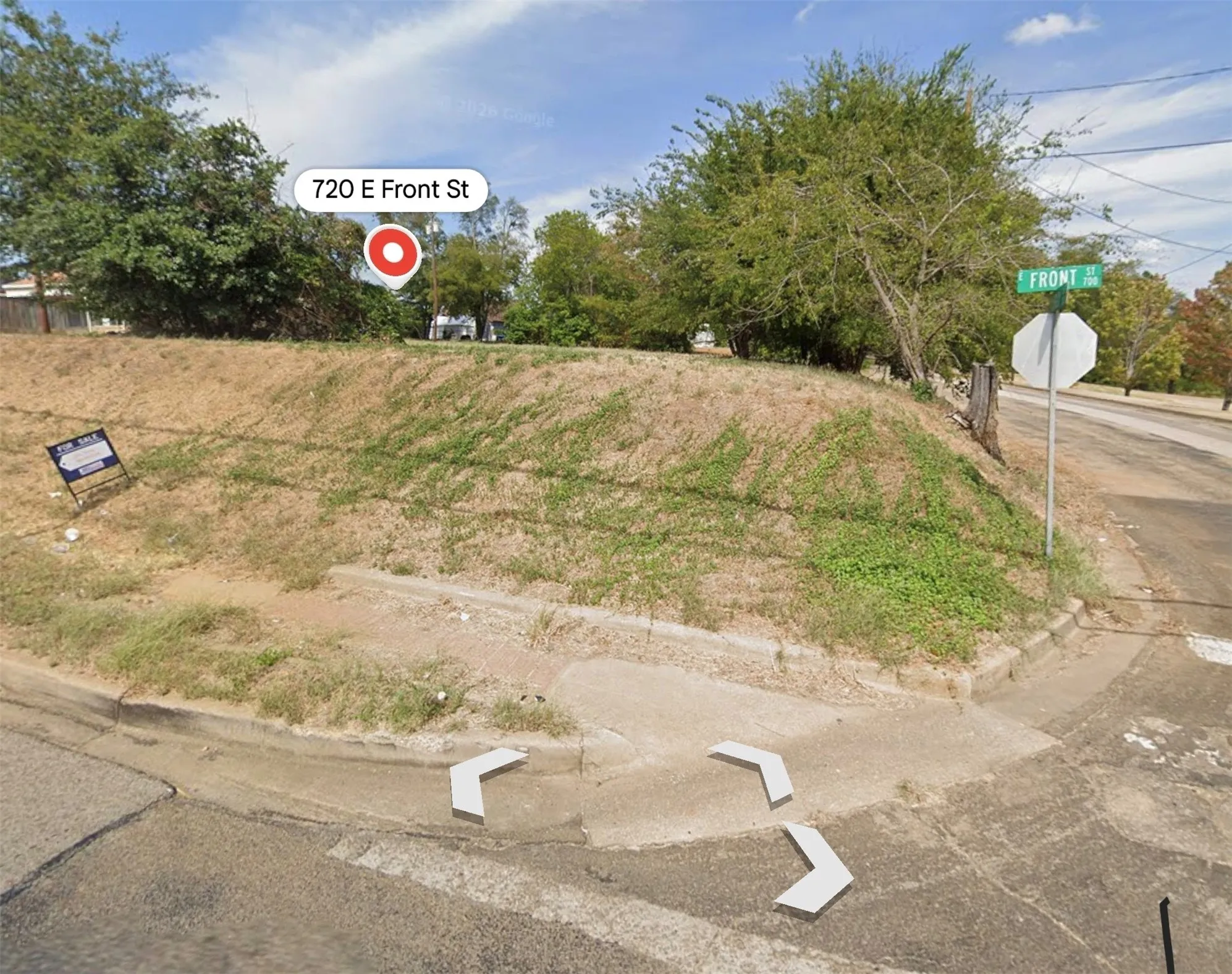 Corner lot featuring street-level concrete curb access, sidewalk infrastructure, and mature trees