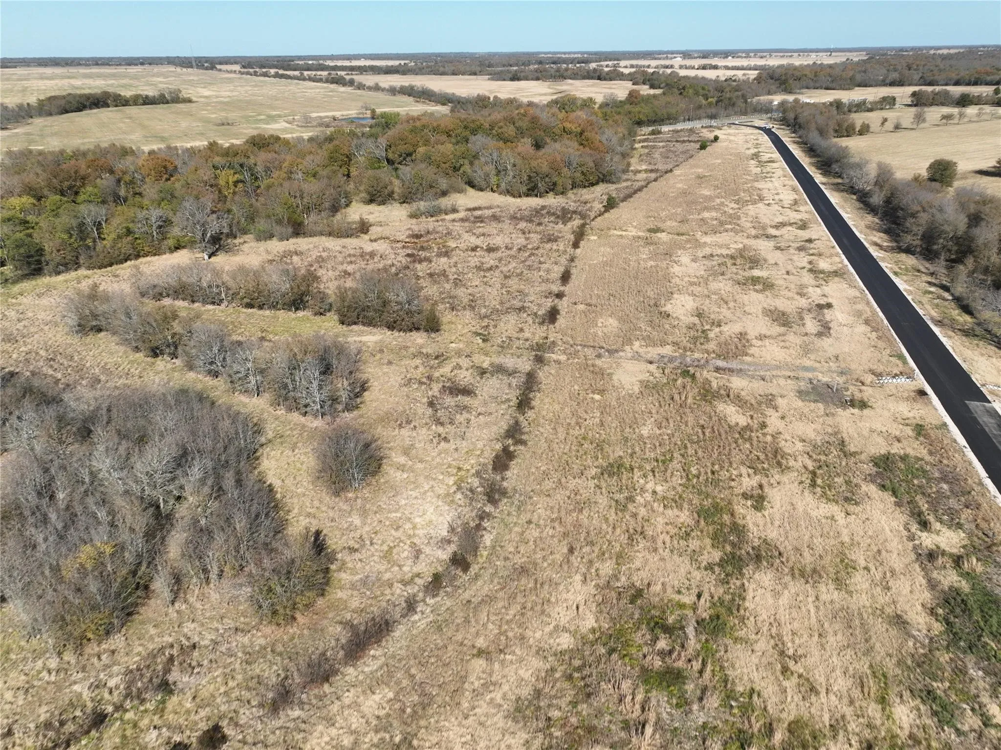 Expansive acreage featuring mature tree lines, open natural terrain, and direct frontage on a paved road