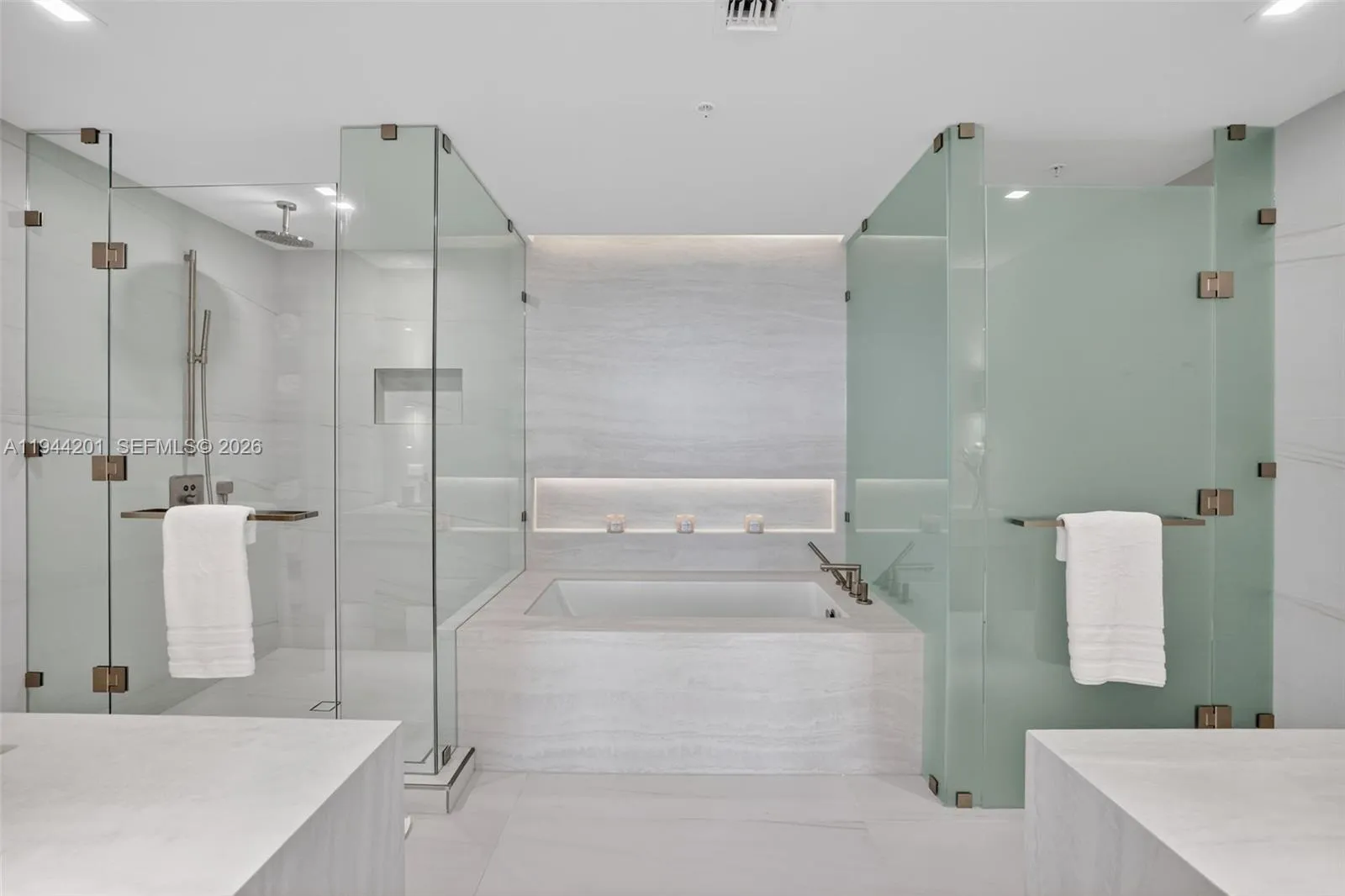 The 06 line primary bath feels like a private spa. Oversized and beautifully proportioned, it features a frameless glass walk in shower, designer soaking tub, dual vanities with stone counters, and sleek modern fixtures. Clean architectural lines, neutral luxury finishes, and generous storage for a calm, resort style retreat that complements the open coastal aesthetic of the residence.