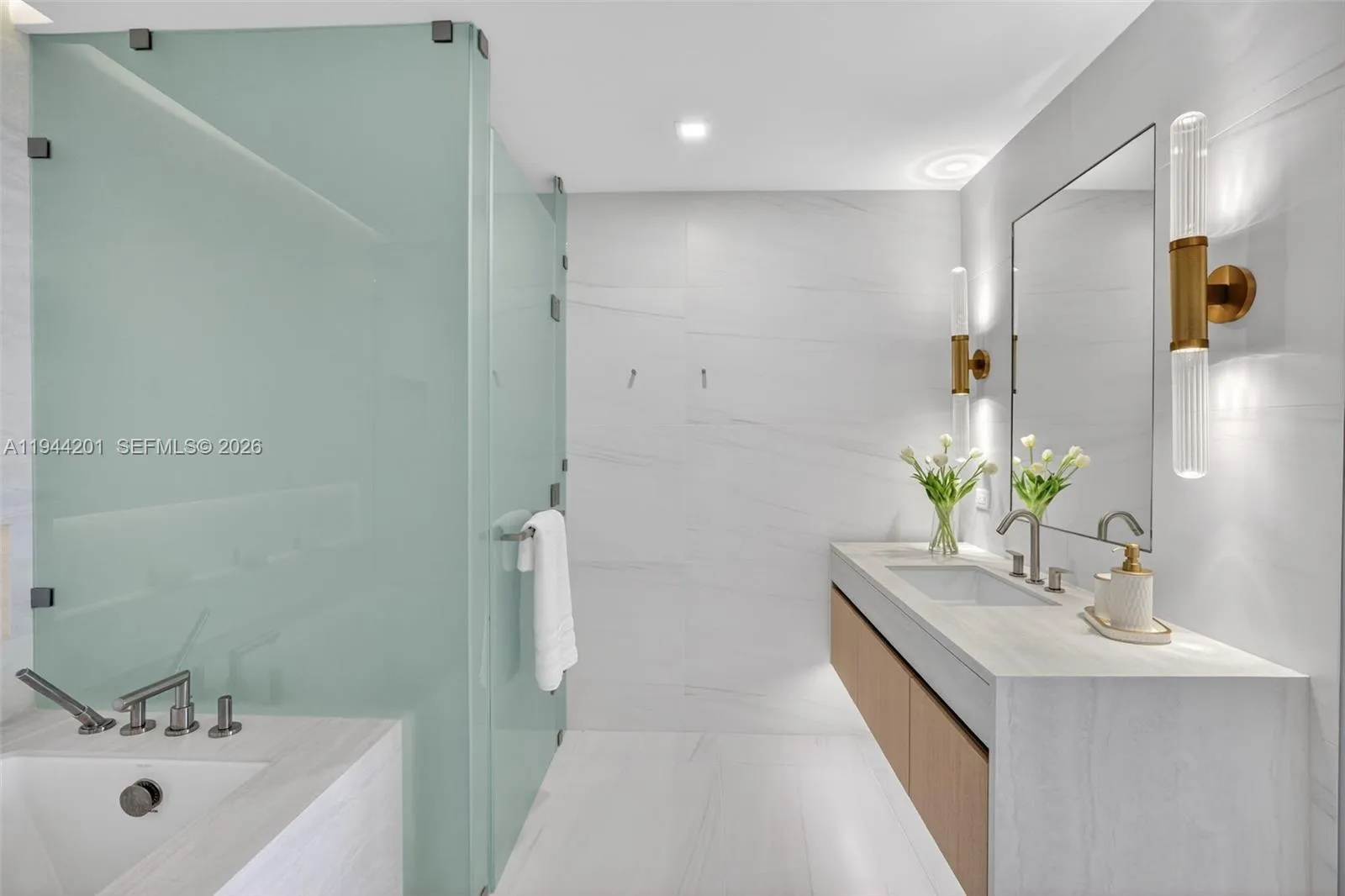 The 06 line primary bath feels like a private spa. Oversized and beautifully proportioned, it features a frameless glass walk in shower, designer soaking tub, dual vanities with stone counters, and sleek modern fixtures. Clean architectural lines, neutral luxury finishes, and generous storage for a calm, resort style retreat that complements the open coastal aesthetic of the residence.