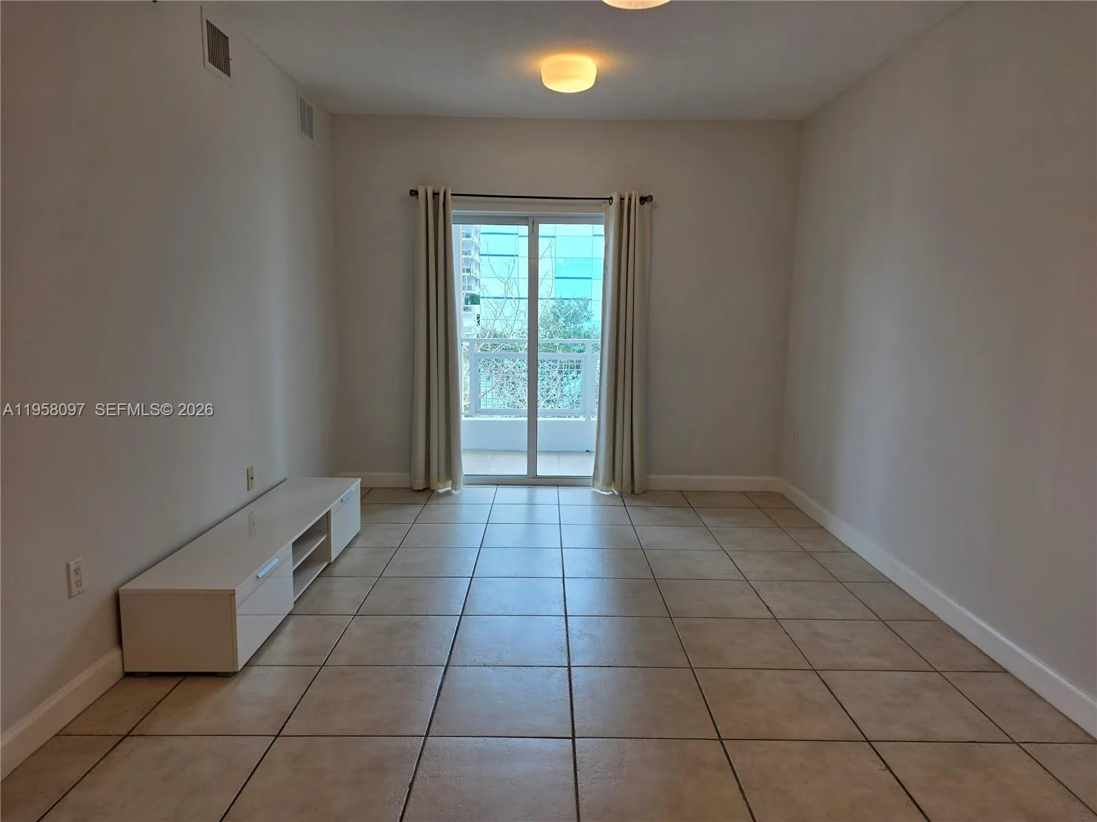Living room with sliding glass doors leading to a private balcony, offering natural light and city surroundings.
