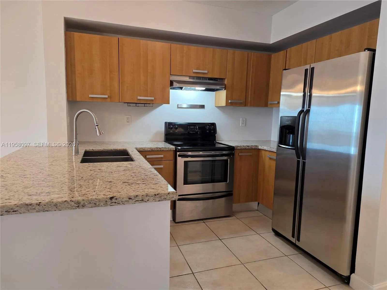 Contemporary kitchen featuring granite countertops, wood cabinetry, stainless steel appliances, and ample storage space.