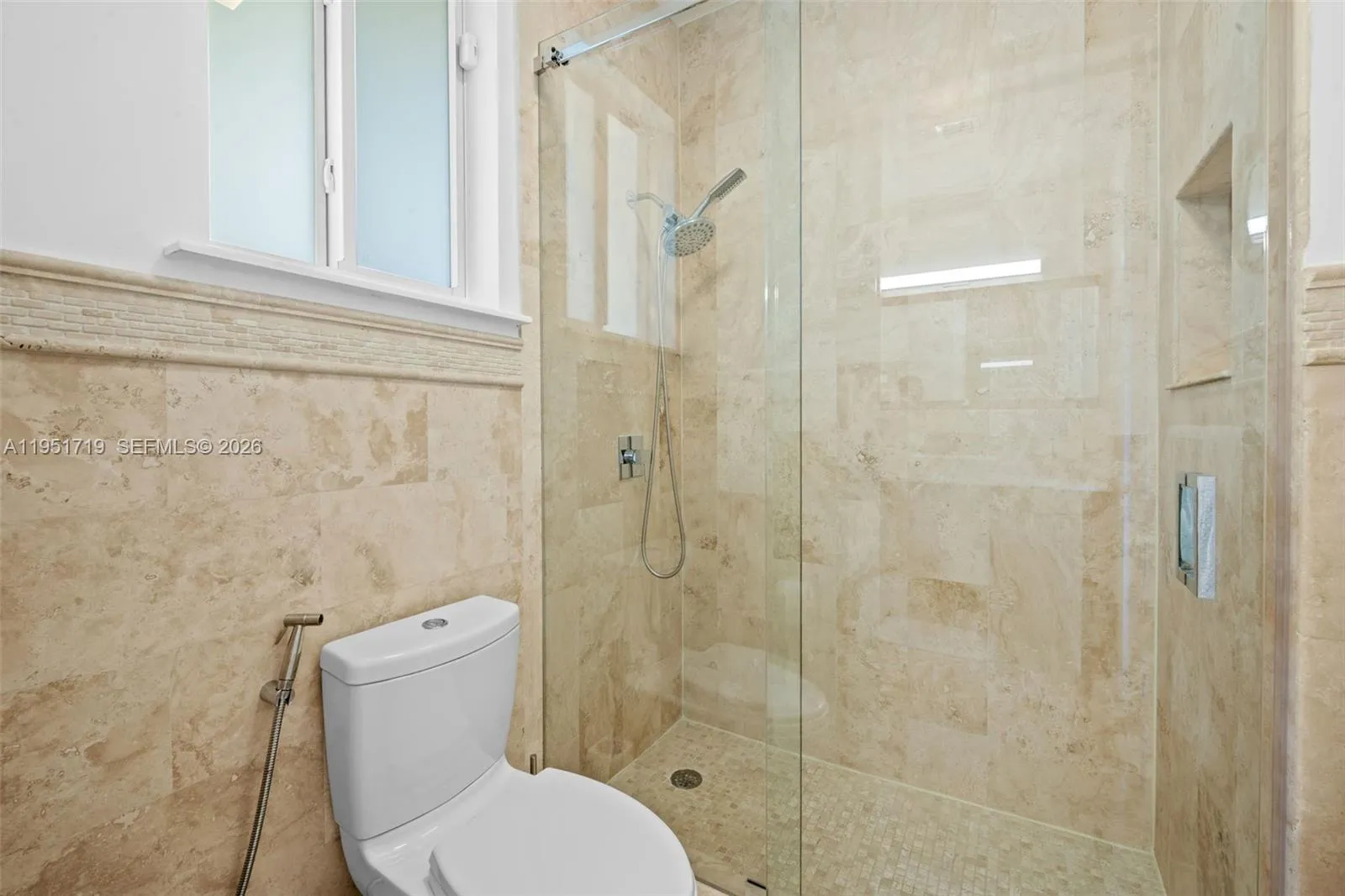 A well-appointed full bath featuring a warm wood vanity with a white vessel sink and a glass-enclosed tub/shower combination.
