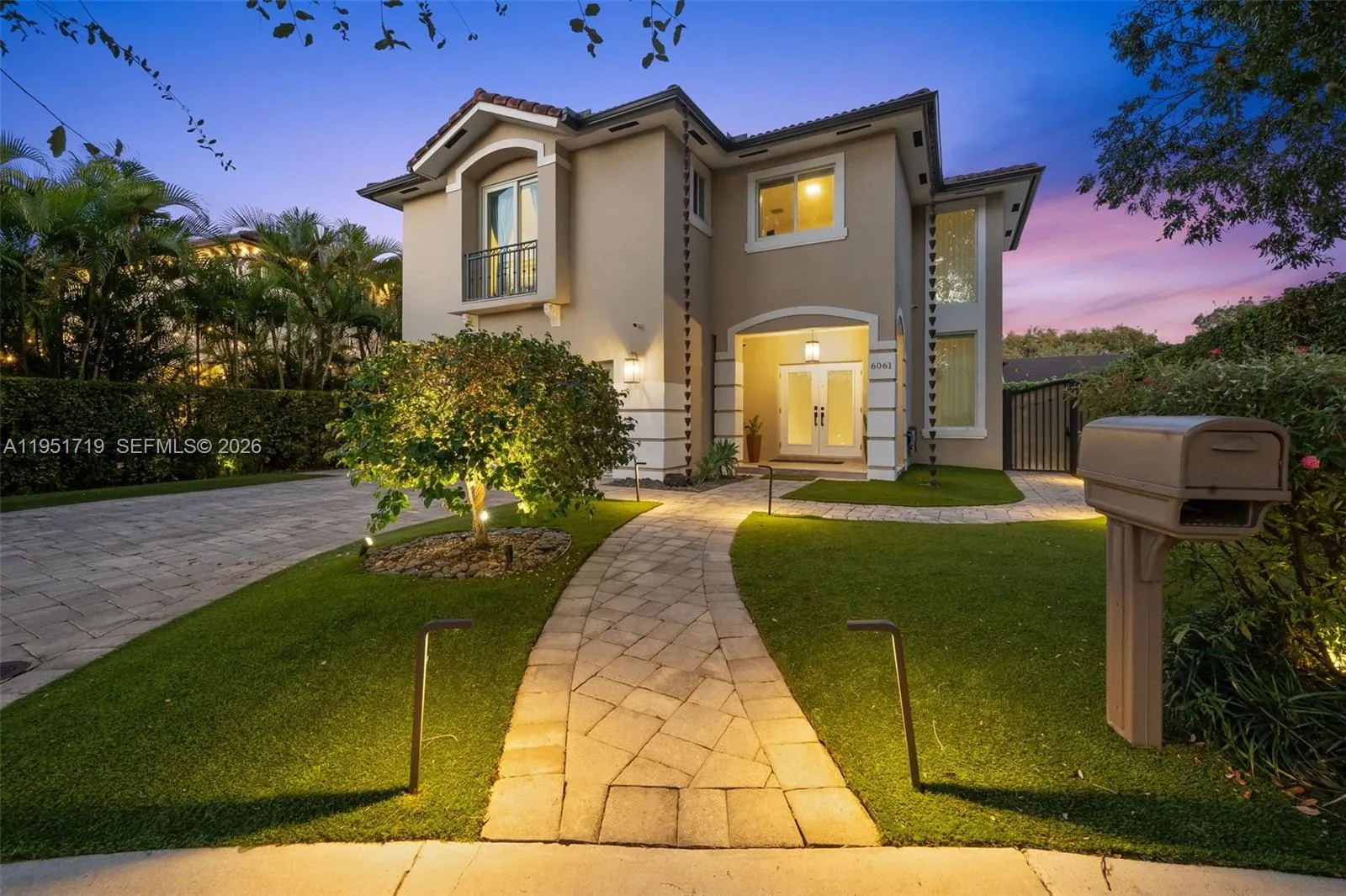 This stunning two-story residence makes a grand impression with contemporary architecture, professionally manicured tropical landscaping, and elegant dusk lighting.