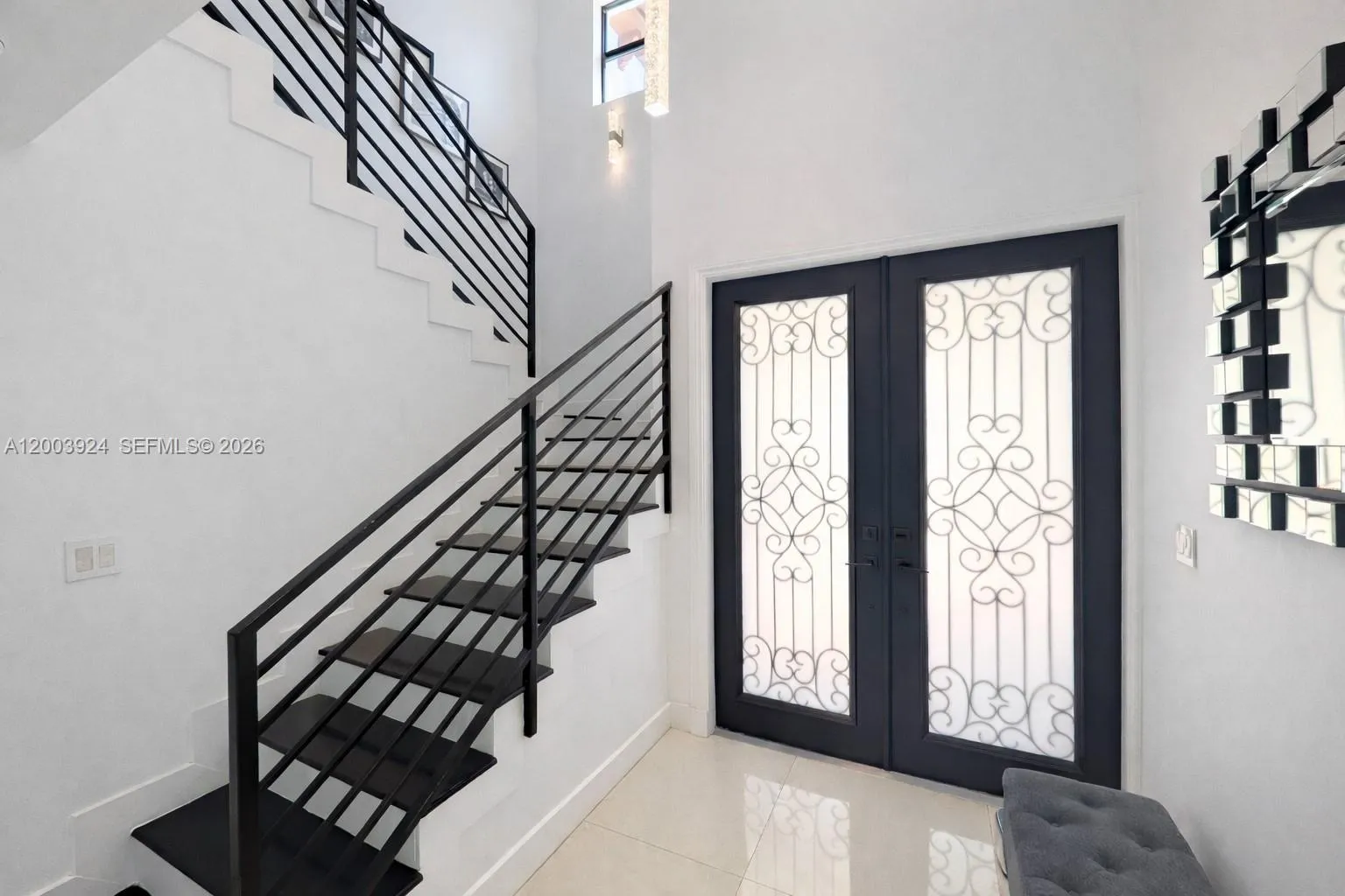 foyer with two-story ceiling, chandelier and translucent French doors providing afternoon light.  storage room under upper stair section