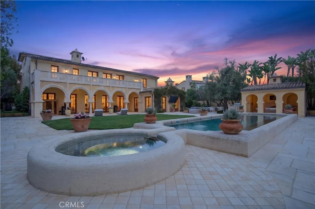 Mediterranean-style home with arched facade, swimming pool, and circular spa at dusk.