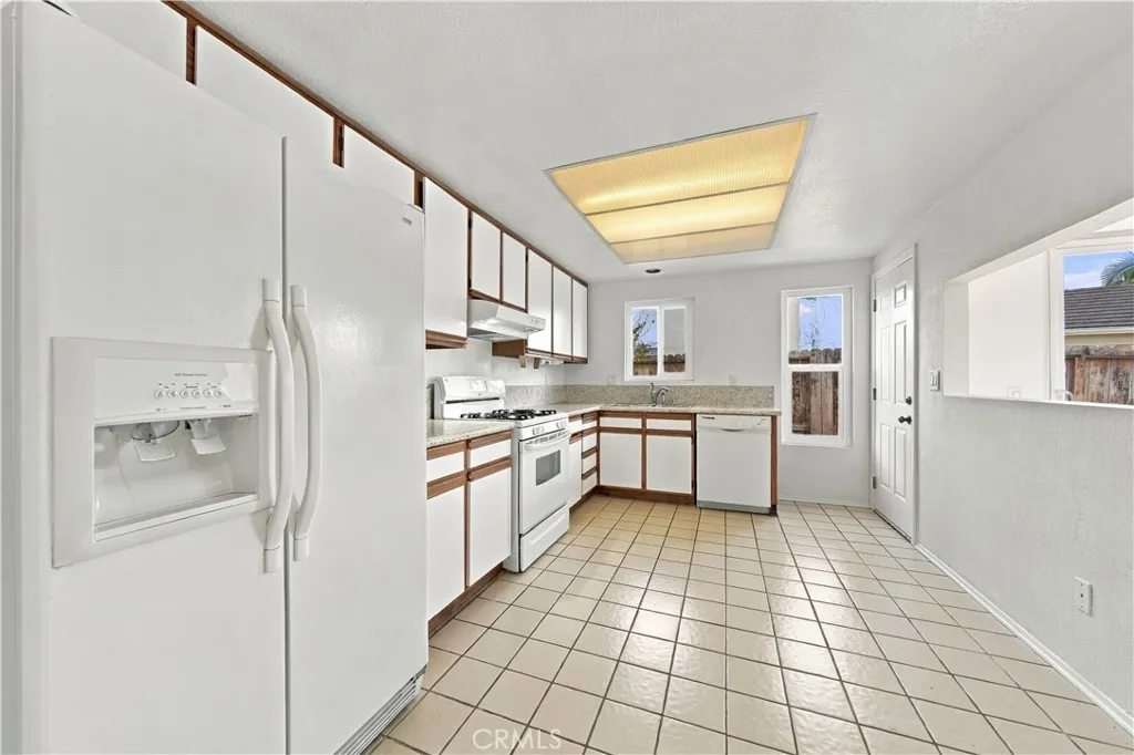 Kitchen w tiled flooring, dual pane windows, door to back patio and pass thru space to dining area on the right.