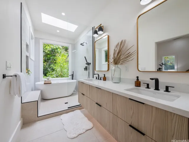 The primary bath is a private sanctuary, exuding spa-like tranquility with nature just outside the window. Lush greenery provides natural privacy and a sense of serenity as you unwind in the deep soaking tub. Thoughtful design details—dual vanities, under-cabinet lighting, high-end fixtures, and organic textures—create a luxurious, restorative atmosphere that blends seamlessly with the beauty of the outdoors.